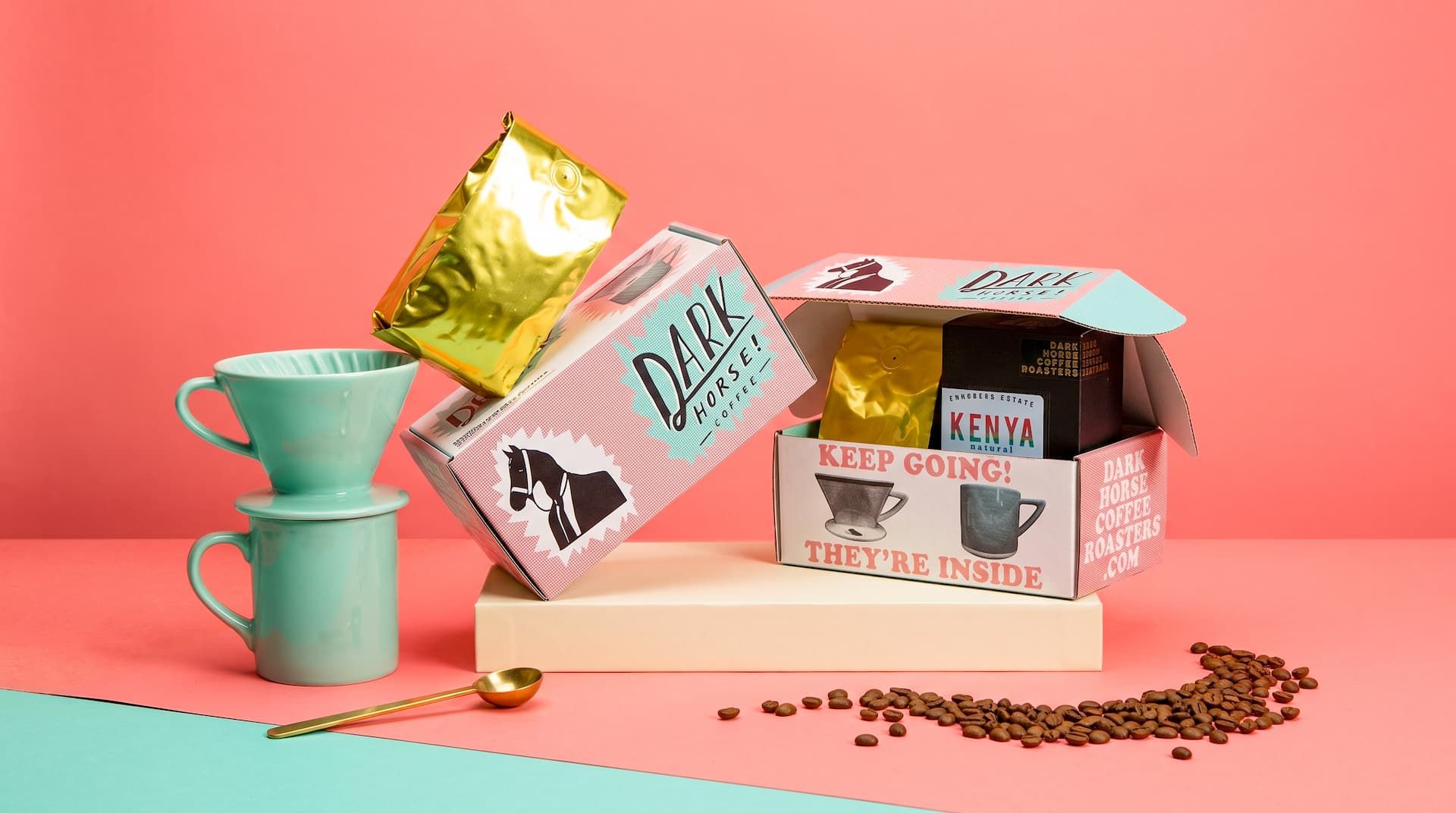 A stylized display of Dark Horse Coffee Roasters packaging, including open and closed boxes, a gold bag, and mint mugs.