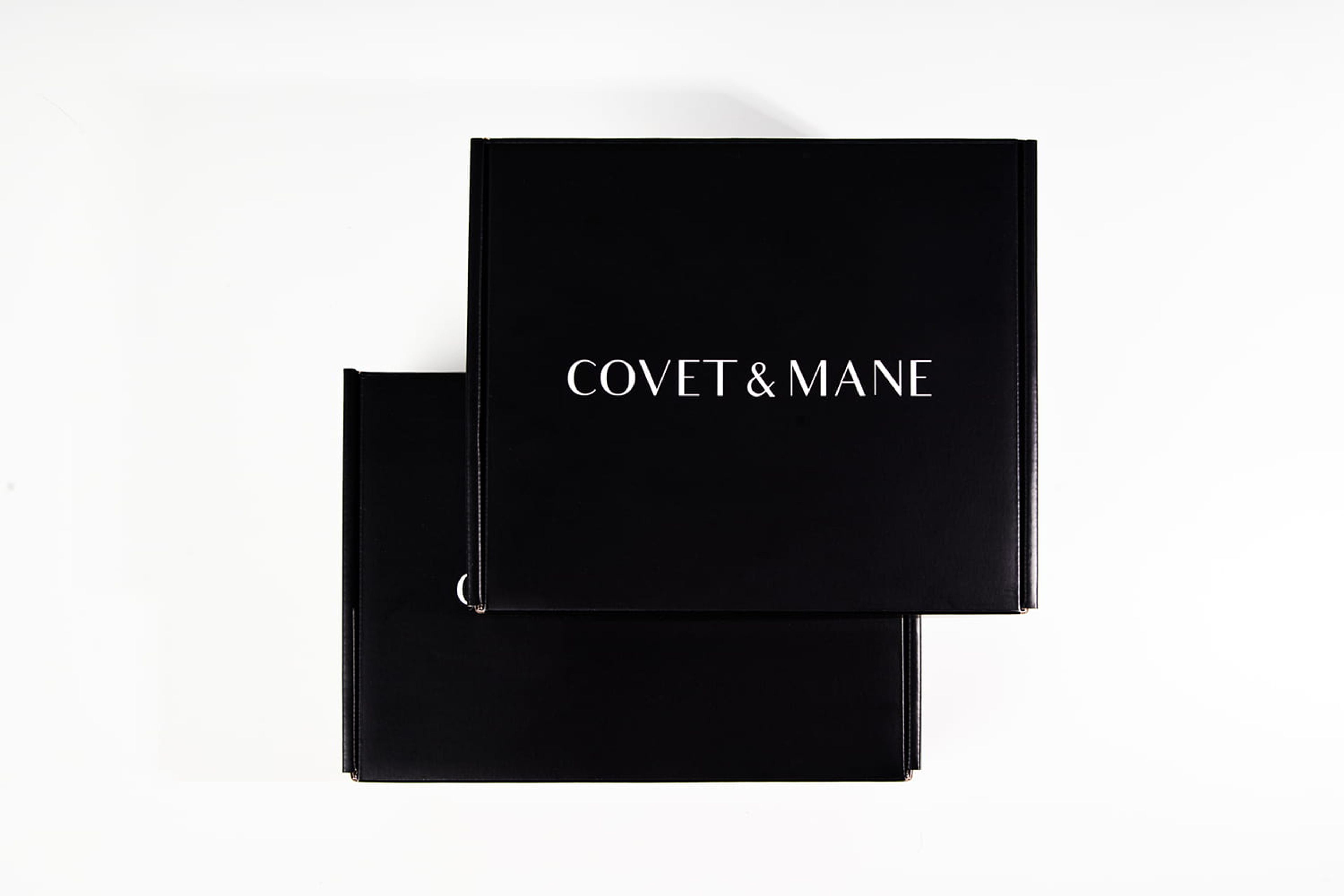 Top-down view of two closed black Covet & Mane mailer boxes stacked slightly offset on a white surface.