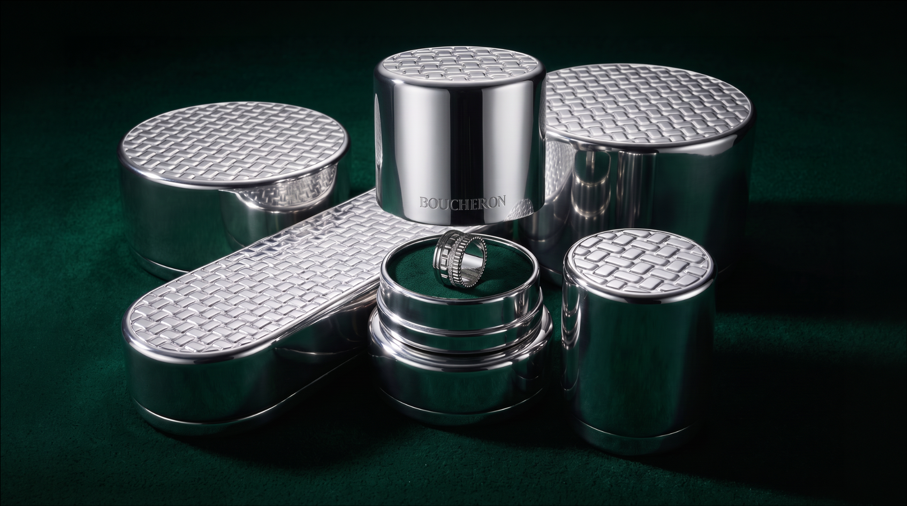 Polished aluminum Boucheron jewelry cases with woven-pattern lids on green velvet, one holding a ring.