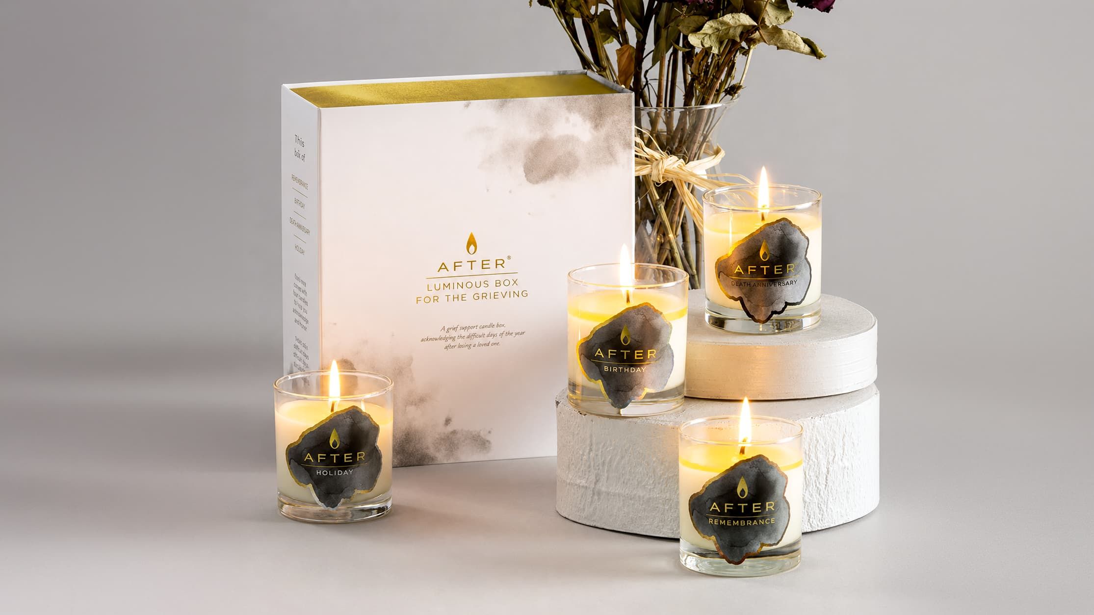 Four lit AFTER milestone candles arranged around the Luminous Box for the Grieving packaging next to dried flowers.