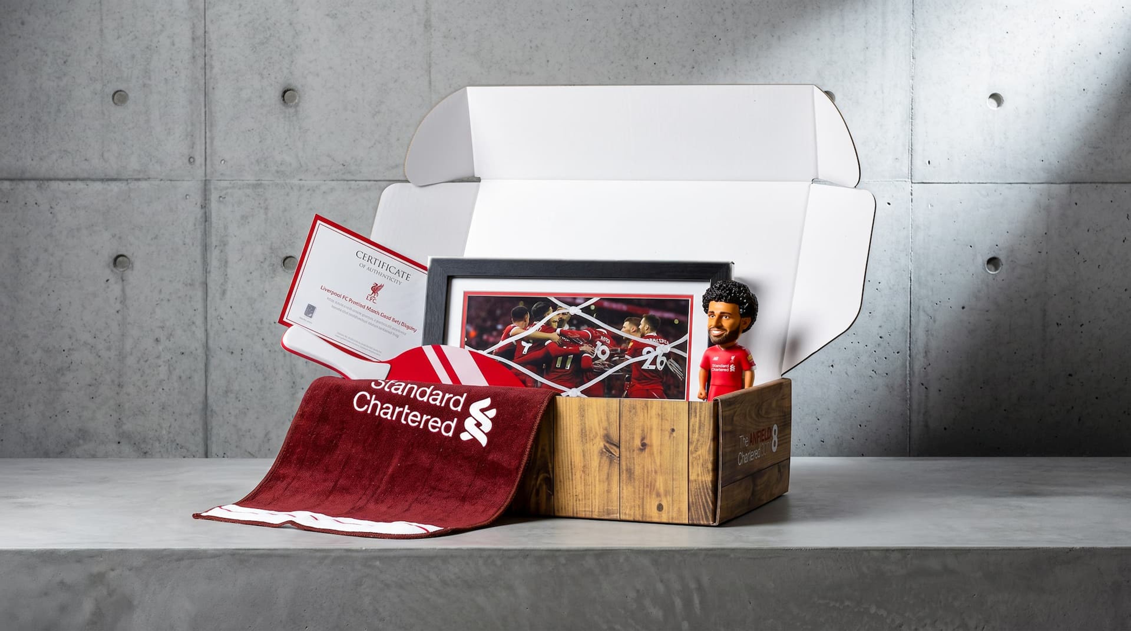 Open Anfield Box revealing Liverpool FC merchandise, including a framed net piece, Salah bobblehead, towel, and certificate.
