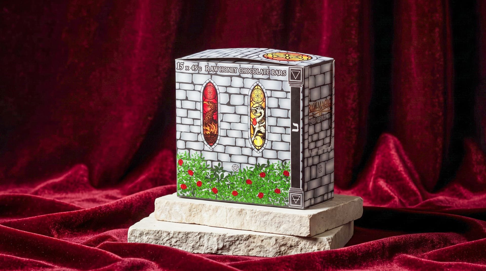 Front view of a Raw Magic Chocolate box showing stained glass Phoenix and Dragon designs, set on stone slabs.