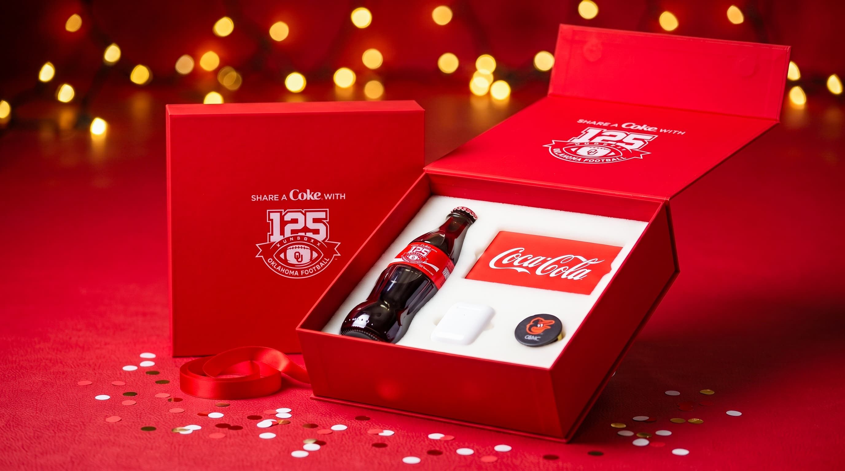 Open red Coca-Cola and Oklahoma Football 125th anniversary gift box holding a glass Coke bottle and custom accessories.