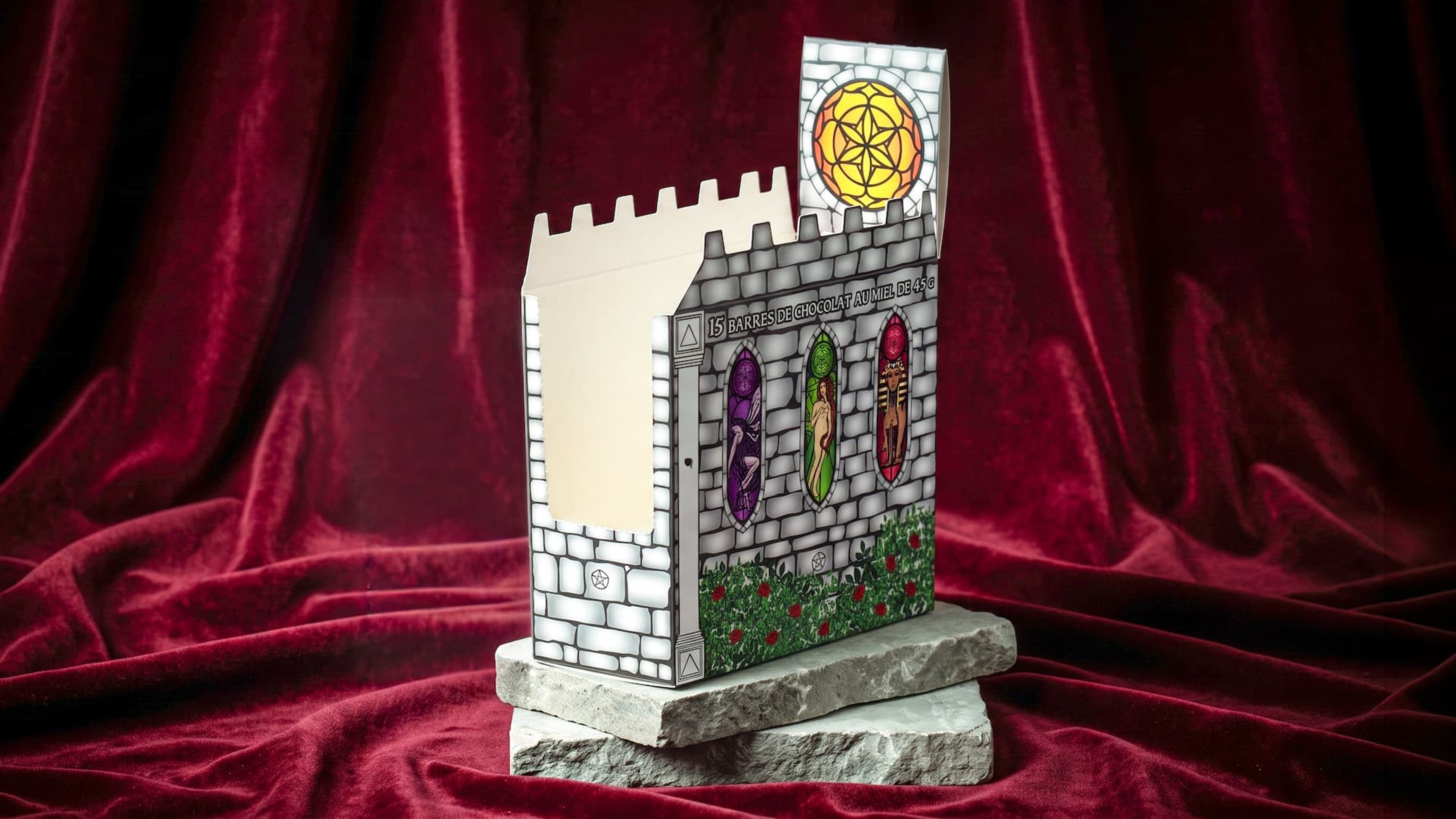 Angled view of an empty castle display box revealing stained glass artwork and a front dispensing cutout on stone.