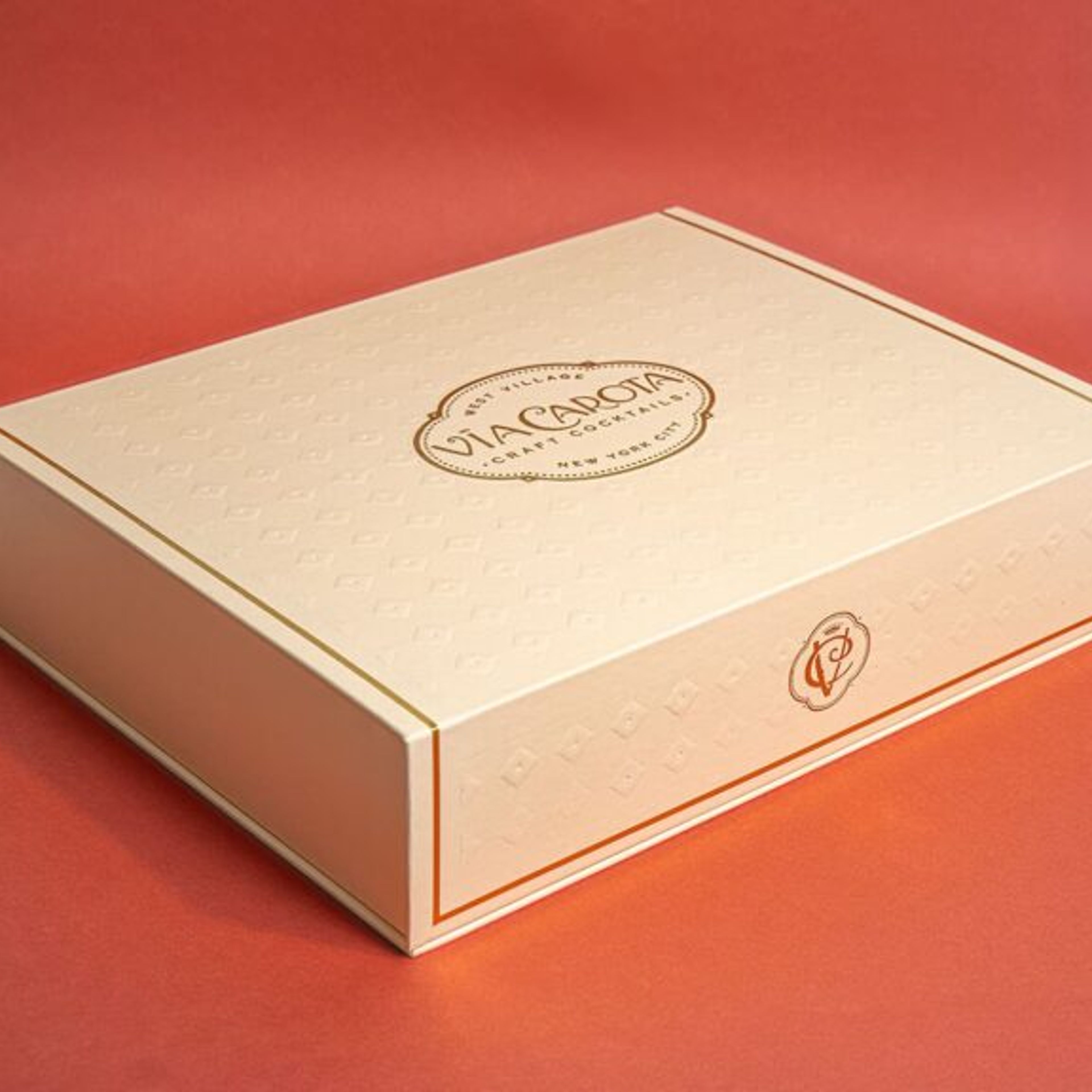 Closed cream Via Carota craft cocktail gift box featuring a central gold foil logo and embossed pattern.