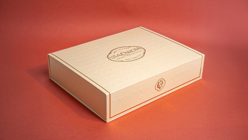 Closed cream Via Carota craft cocktail gift box featuring a central gold foil logo and embossed pattern.