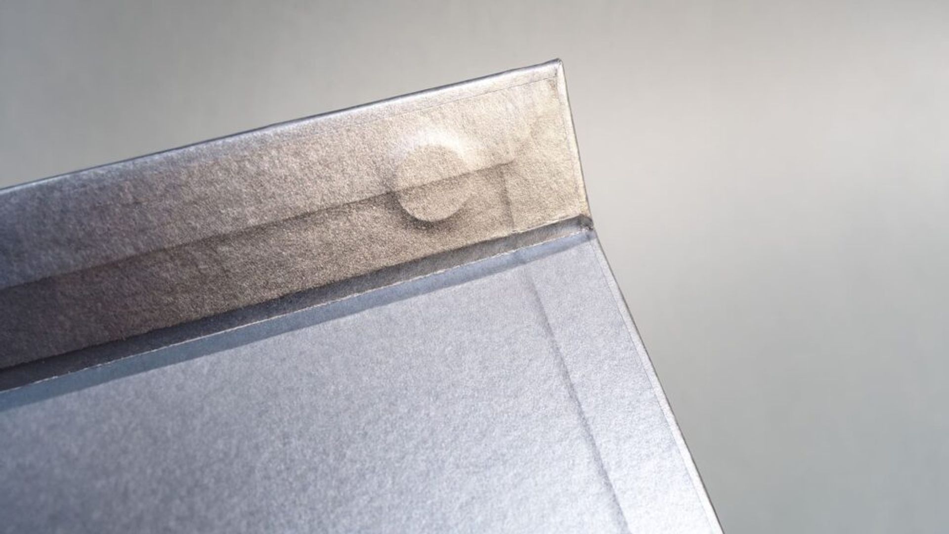 Close-up of the inside flap of a silver box, revealing the subtle raised outline of a circular magnet concealed beneath the paper lining.