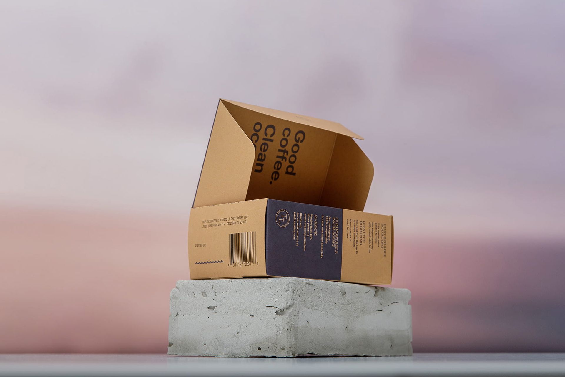 An open Tideline coffee box balanced on a grey concrete block against a pink and purple sunset sky.