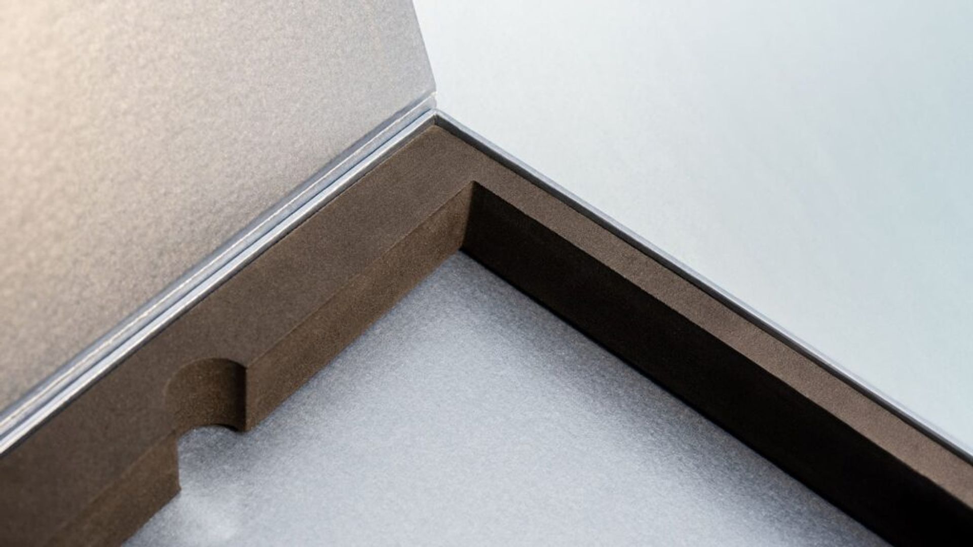 Close-up view inside an open silver box, focusing on a black velvet-lined foam insert featuring a smooth thumb cutout.