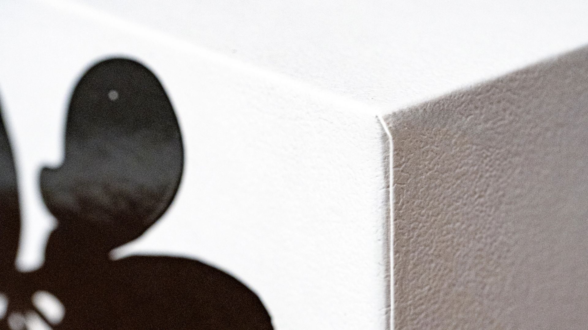 An extreme close-up of a white box corner, highlighting the textured paper and a partial glossy black rounded graphic on the side.