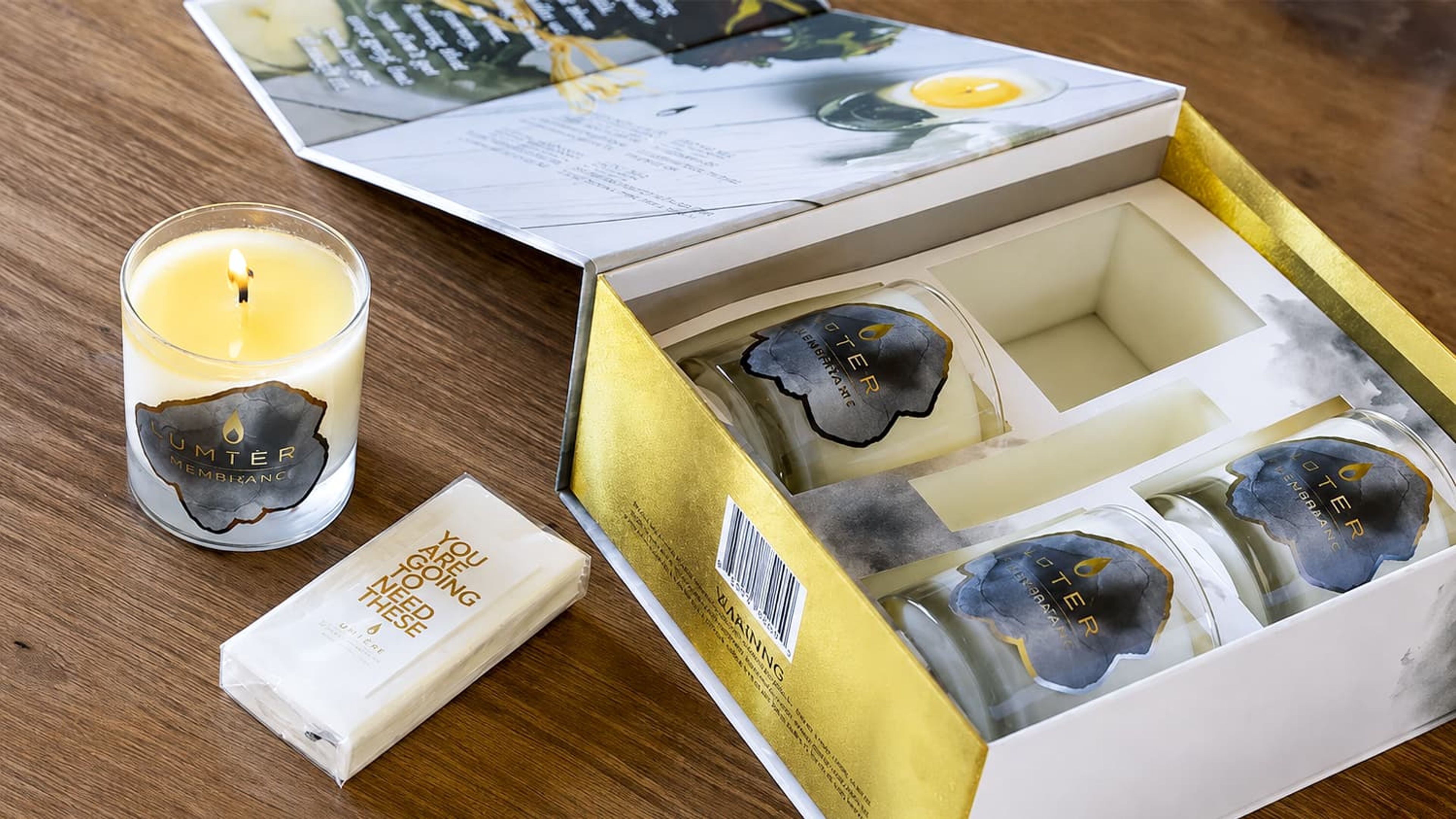 Open Luminous Box revealing a box insert, with one lit candle and a tissue pack resting outside on a wooden table.