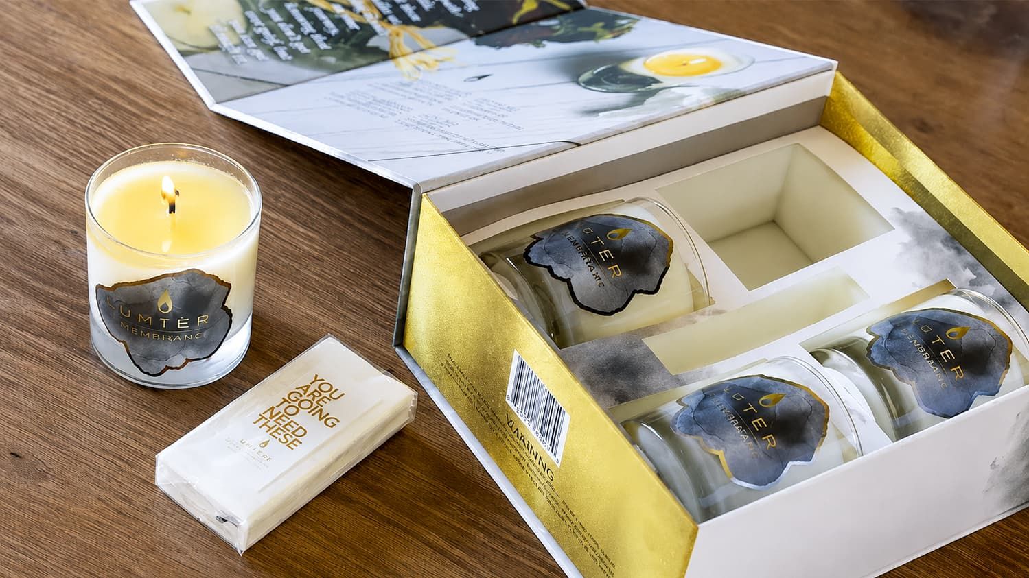 Open Luminous Box revealing a box insert, with one lit candle and a tissue pack resting outside on a wooden table.