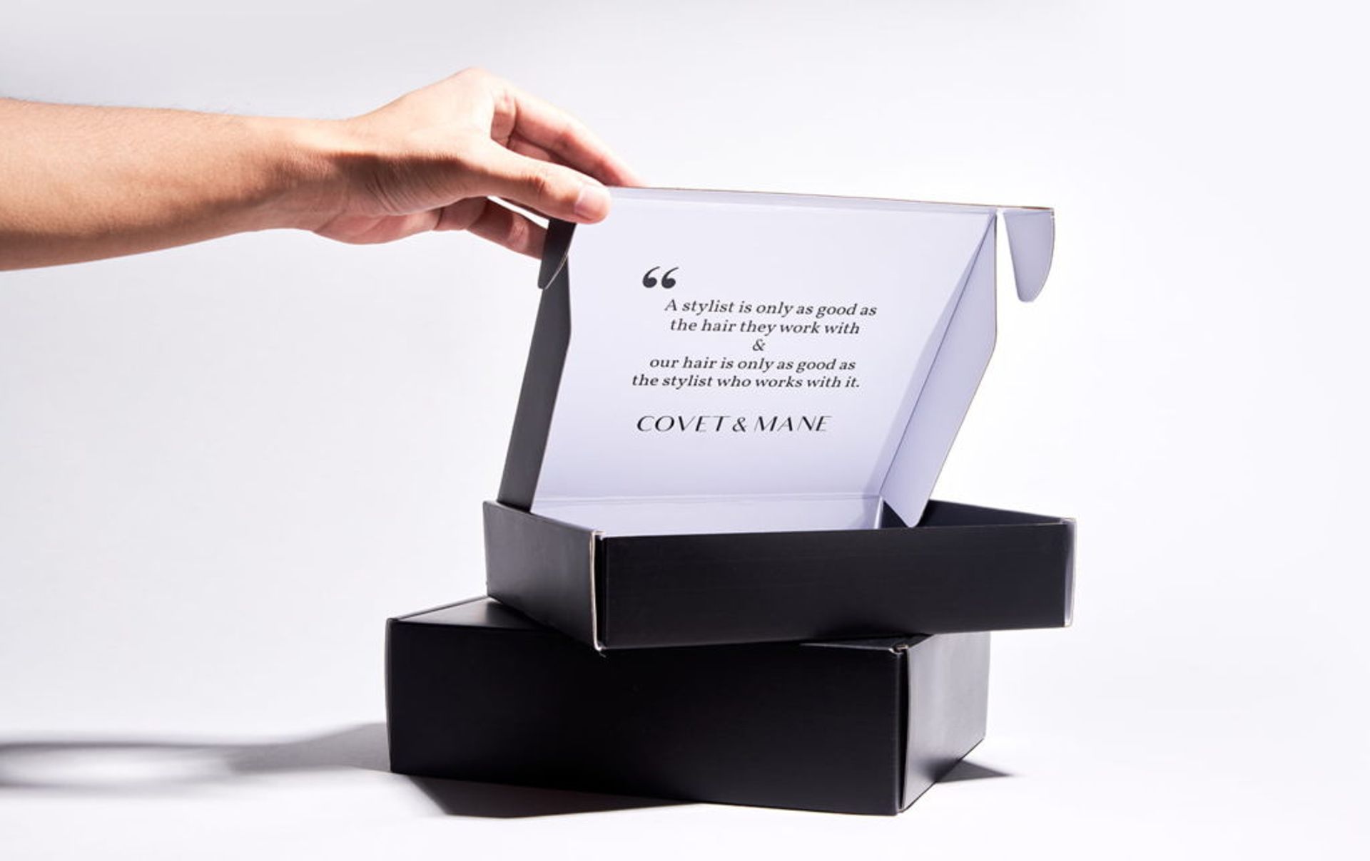 A hand opening a black Covet & Mane mailer box, revealing a printed inspirational quote on the white inner lid.