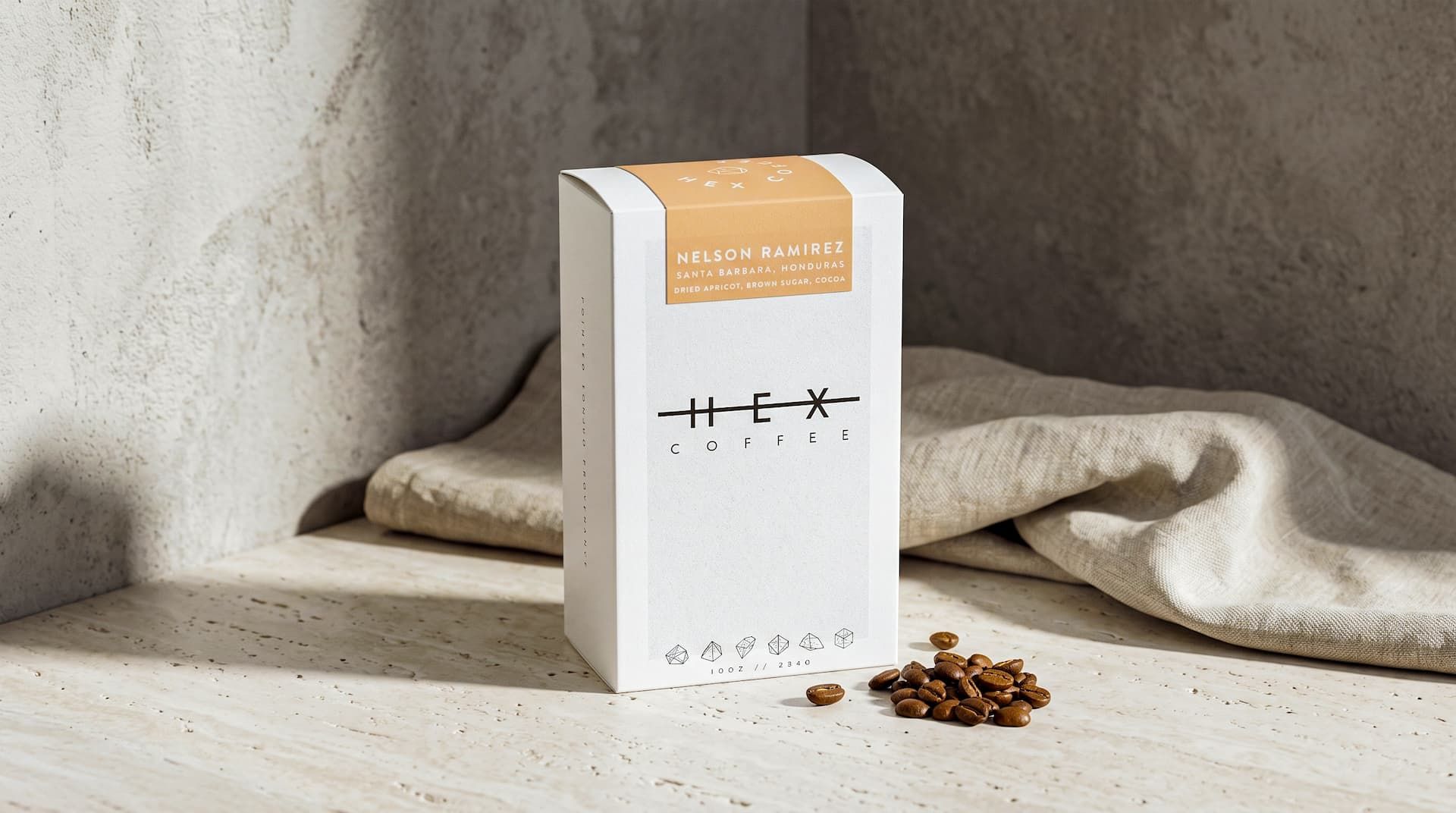 A single Hex Coffee box with an orange Nelson Ramirez label on a stone surface, next to scattered coffee beans and linen.