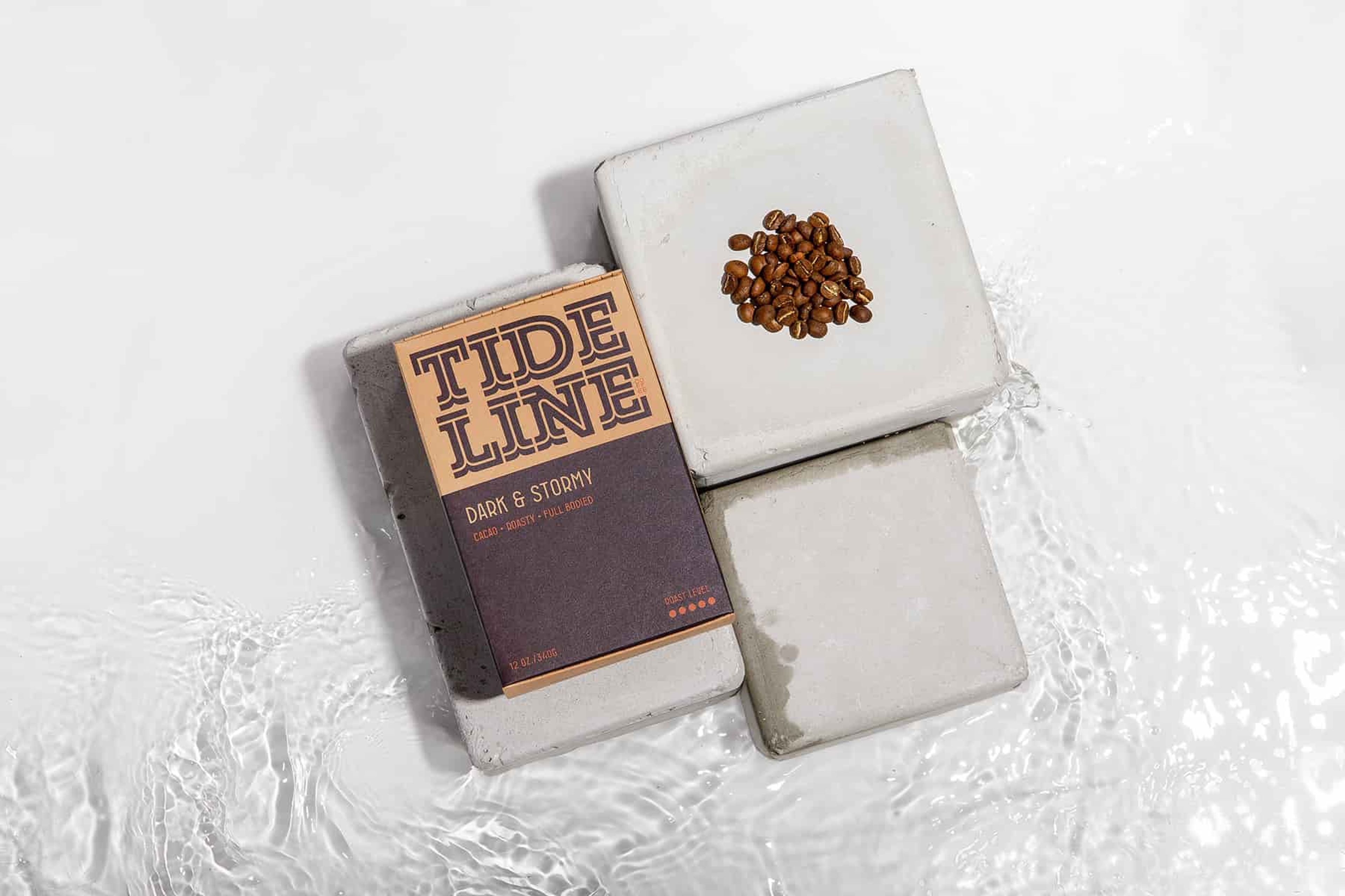 Tideline Dark & Stormy coffee box and a small pile of coffee beans arranged on concrete blocks in water.
