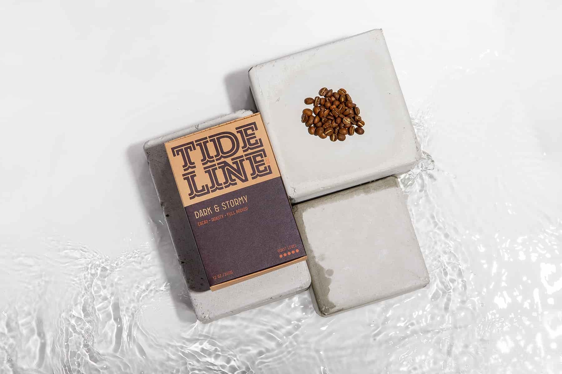 Tideline Dark & Stormy coffee box and a small pile of coffee beans arranged on concrete blocks in water.