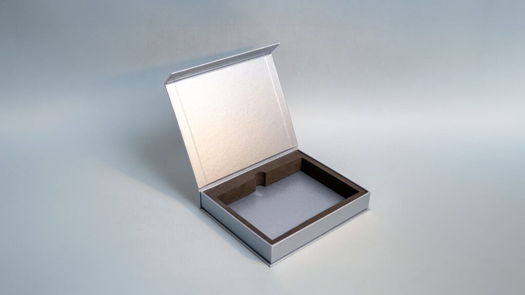 An open silver presentation box showcasing its hinged lid, metallic interior lining, and custom dark brown insert frame.