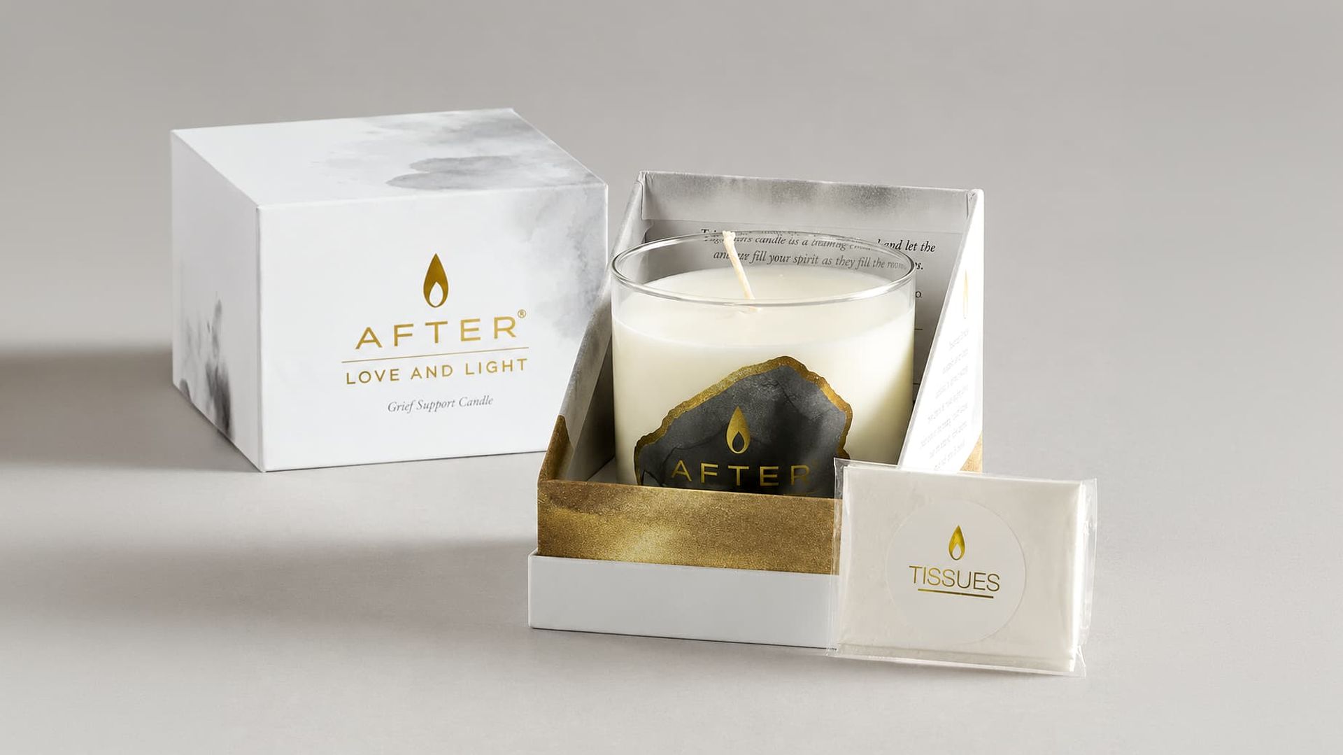 Open AFTER Love and Light box displaying a glass candle inside a gold-rimmed base next to a small tissue pack.