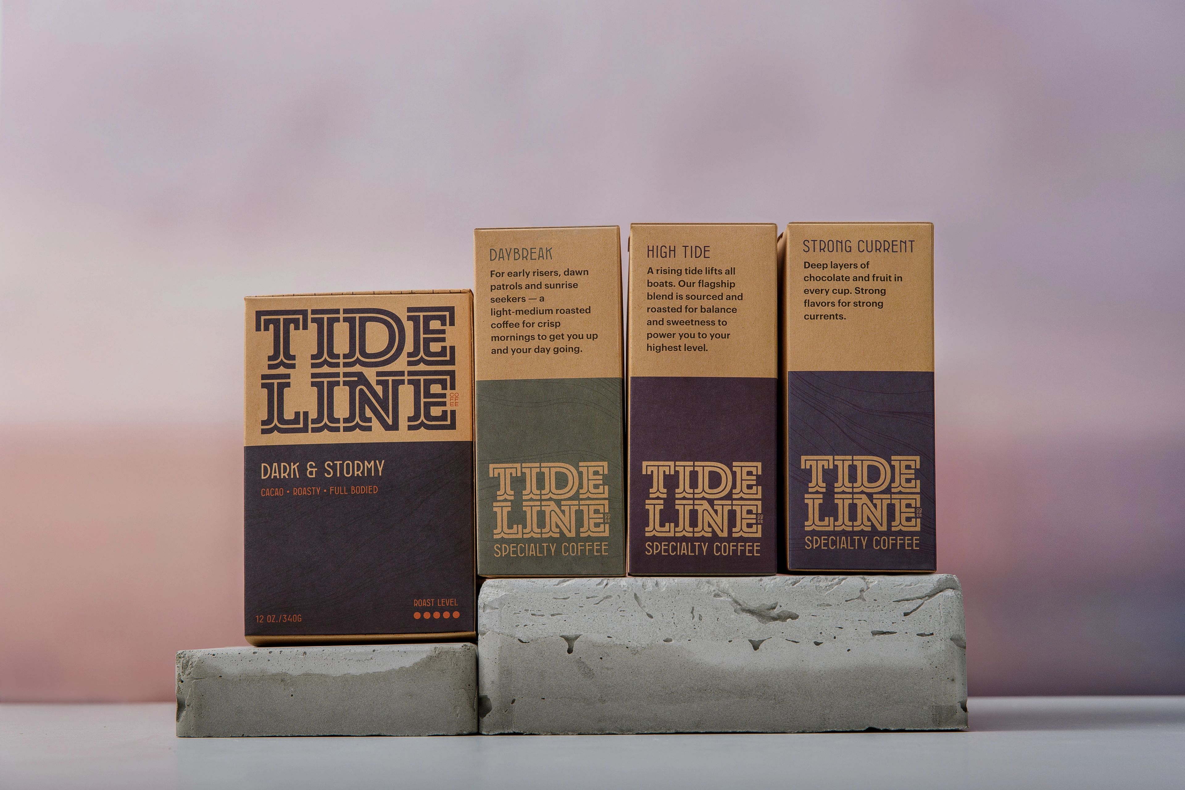 Four Tideline specialty coffee boxes arranged on stacked concrete blocks against a pastel sunset sky.