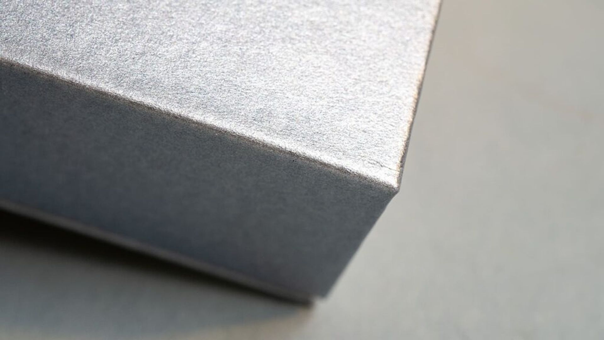 Macro close-up photograph showing the sharp, precision-folded corner of a custom presentation box made from textured metallic silver paper.
