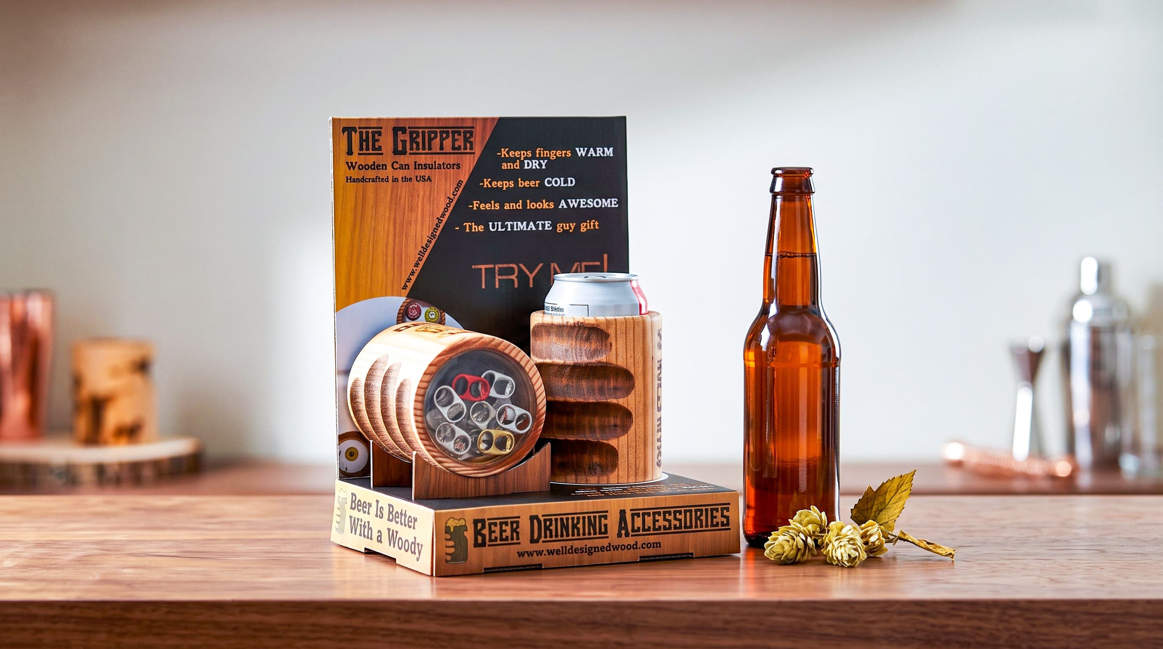 Retail display for Well Designed Wood's wooden can insulators holding two wooden koozies, next to a beer bottle and hops.