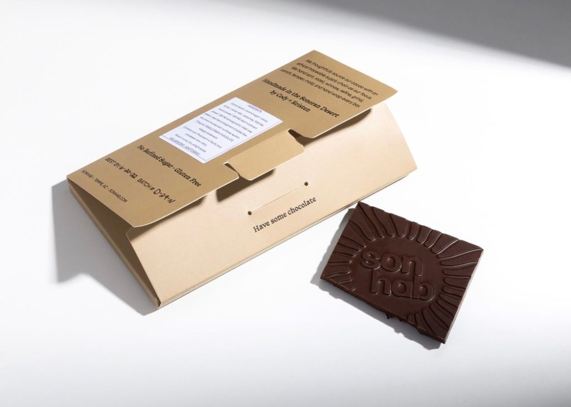 An open Sonhab chocolate wrapper laying flat next to a molded chocolate bar featuring a sunburst logo design.