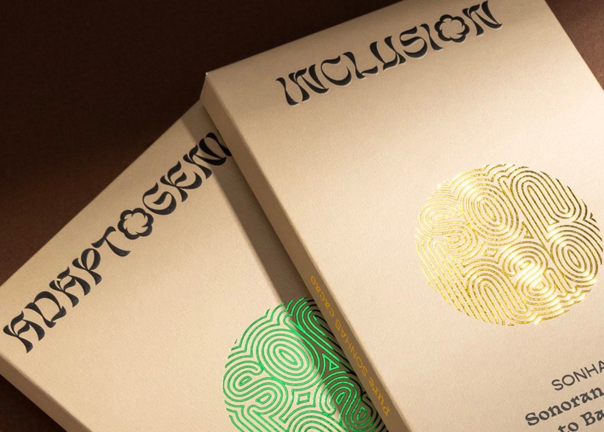 Two Sonhab chocolate boxes, Adaptogenic and Inclusion, featuring intricate green and gold foil-stamped logos.