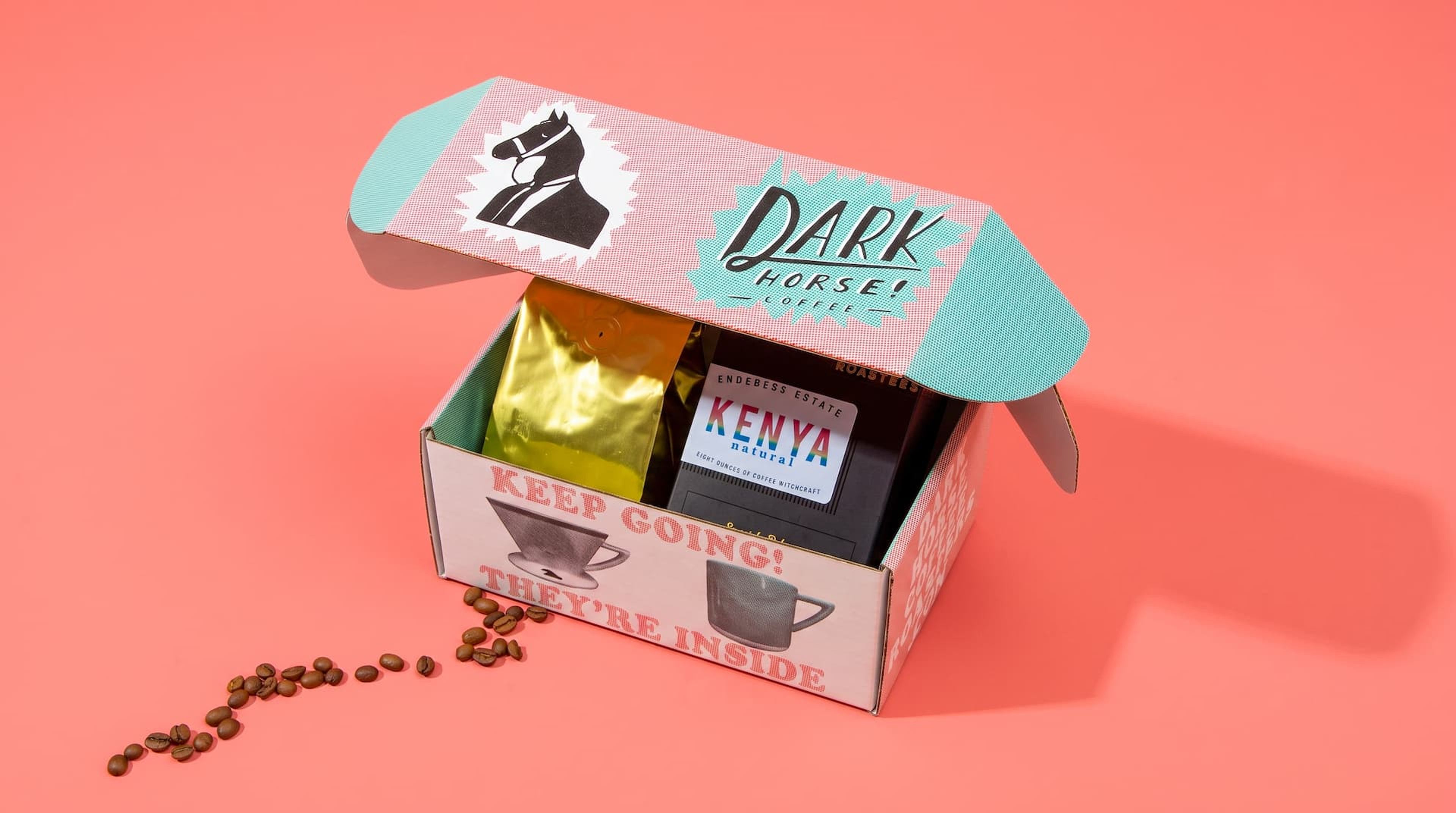 High-angle view of an open Dark Horse mailer box revealing interior graphics, a gold coffee bag, and a black Kenya box.