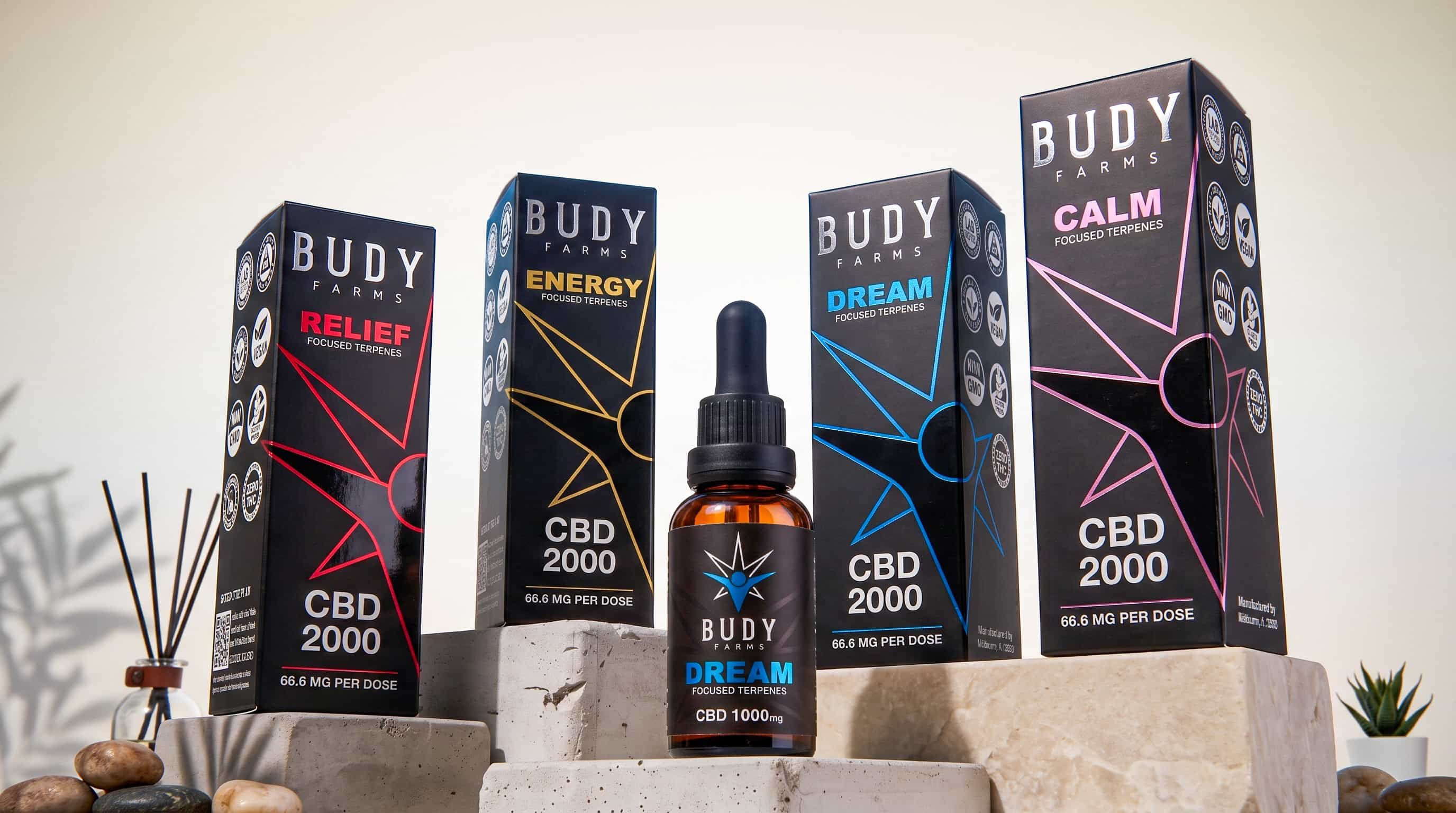 Four Budy Farms CBD boxes and a Dream dropper bottle displayed on stacked concrete blocks.