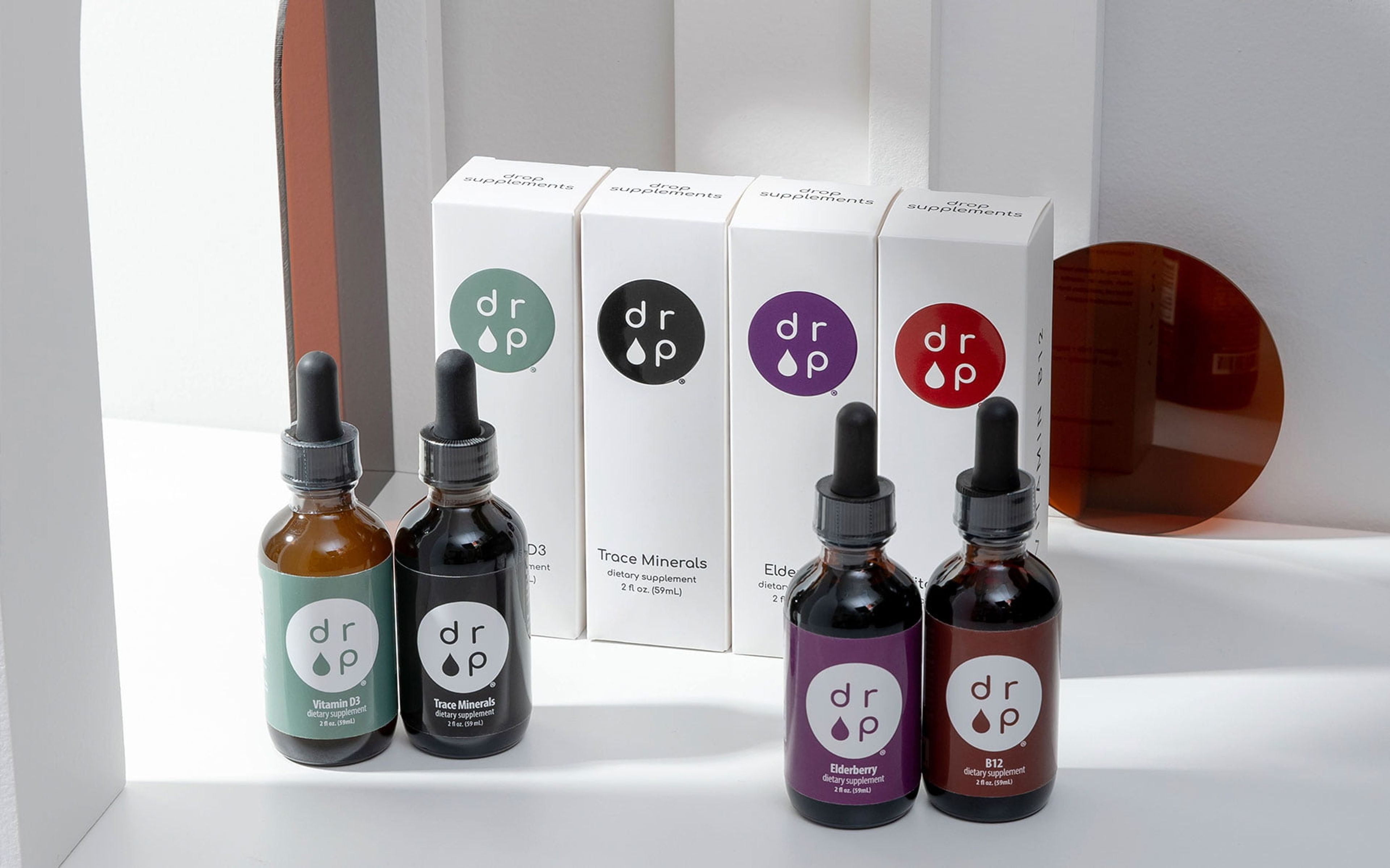 Four Drop Supplement dropper bottles standing in front of their corresponding white folding cartons.