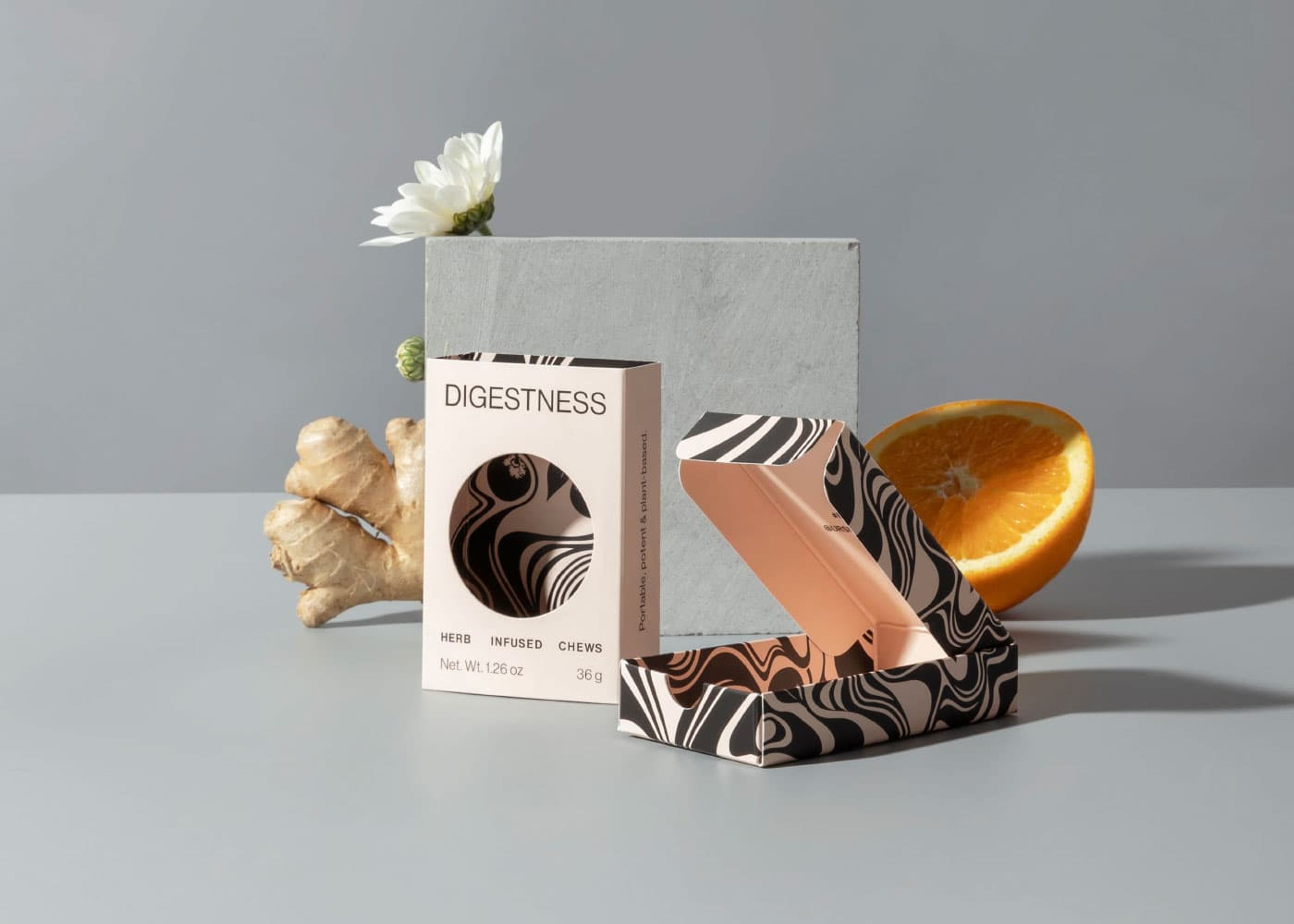A closed Digestness HRBLS box next to an open patterned box, styled with ginger, an orange, and flowers.