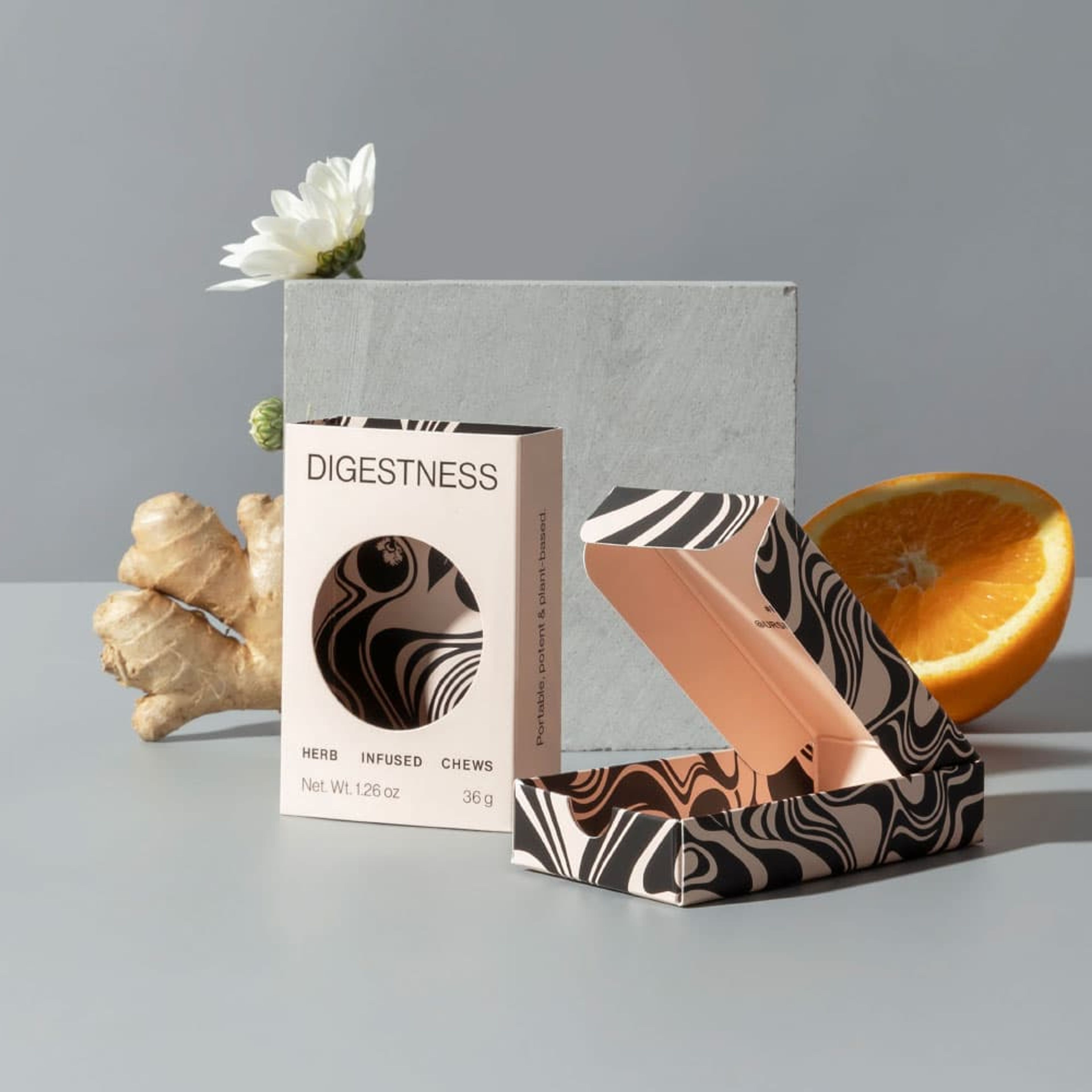 A closed Digestness HRBLS box next to an open patterned box, styled with ginger, an orange, and flowers.