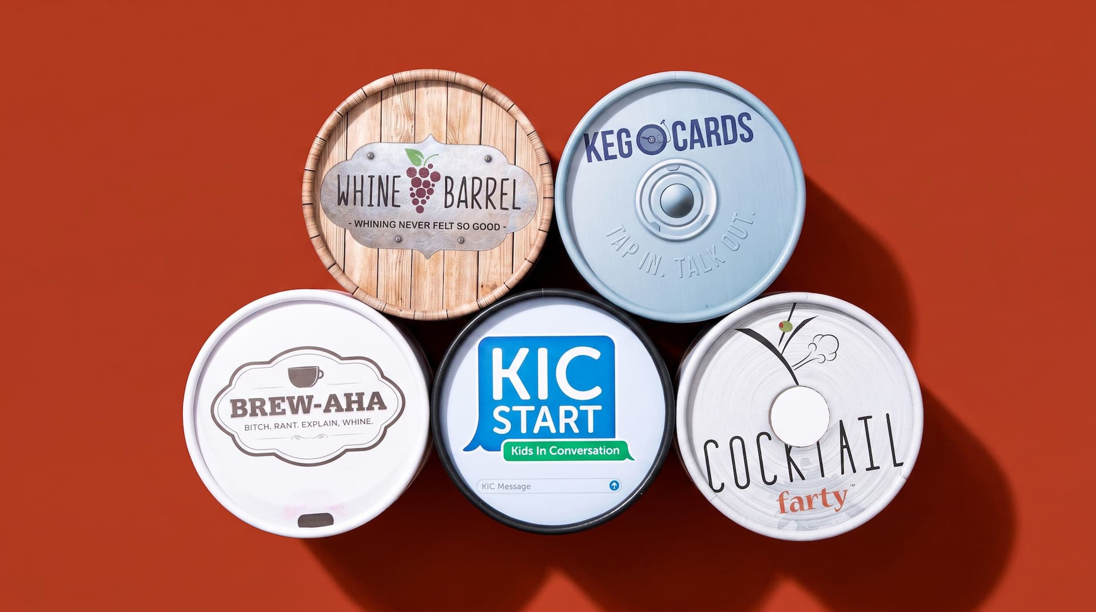 Top-down view of five custom printed circular lids for conversation card games arranged on a terracotta background.