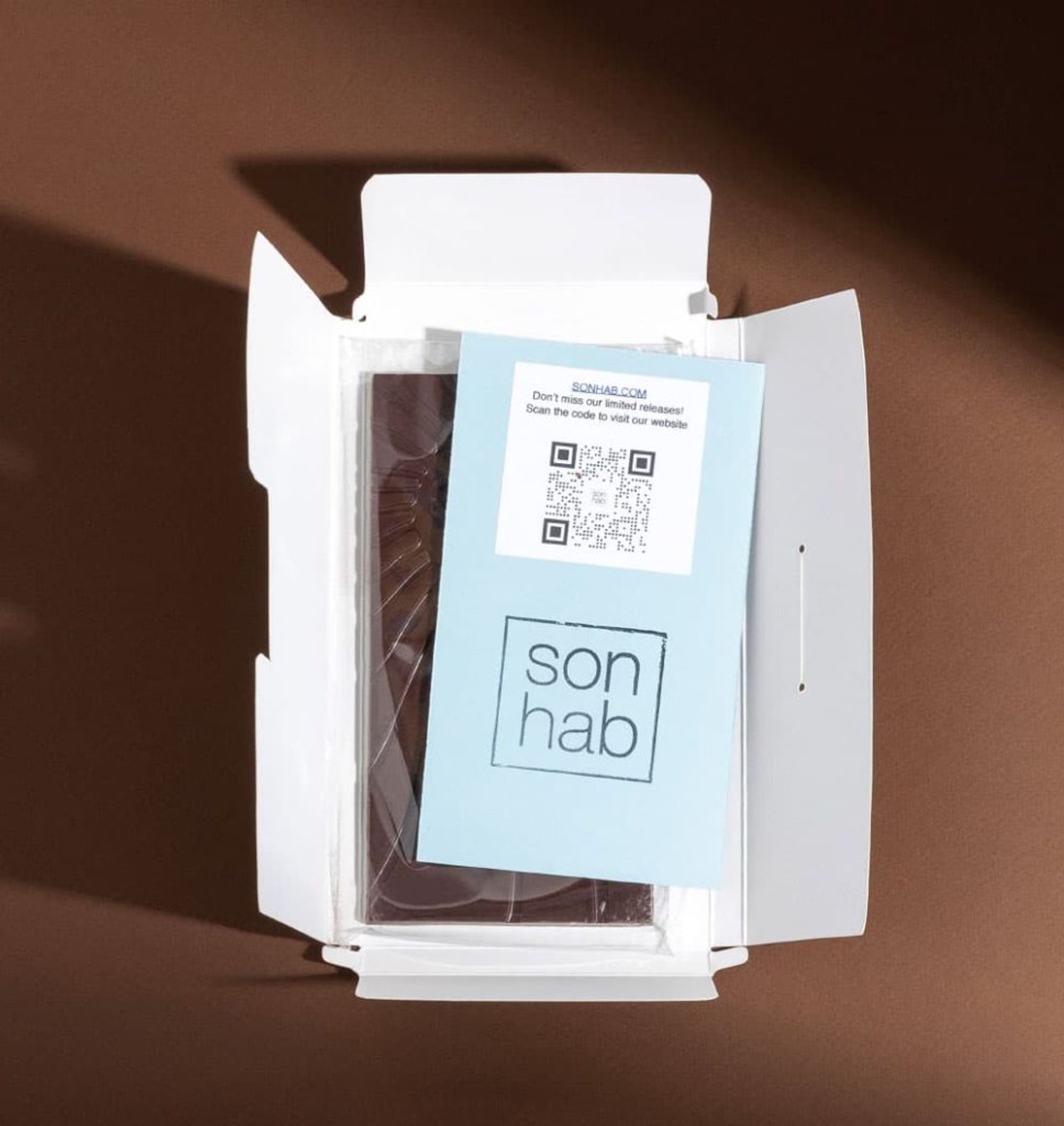 Open white mailer box revealing a Sonhab chocolate bar and a blue informational QR code insert card.