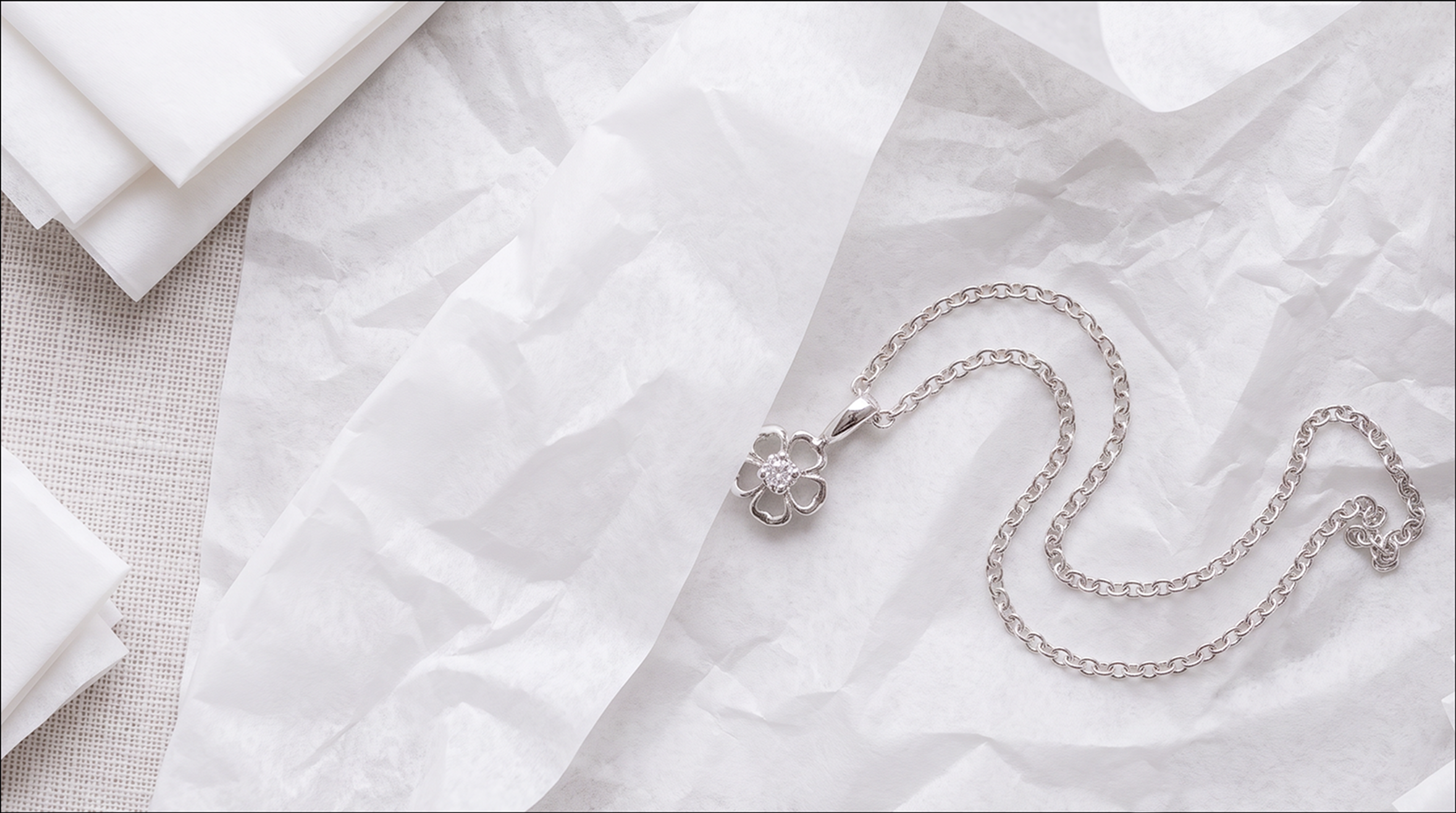 Silver pendant necklace lying on crumpled white tissue paper beside a stack of folded tissue sheets.