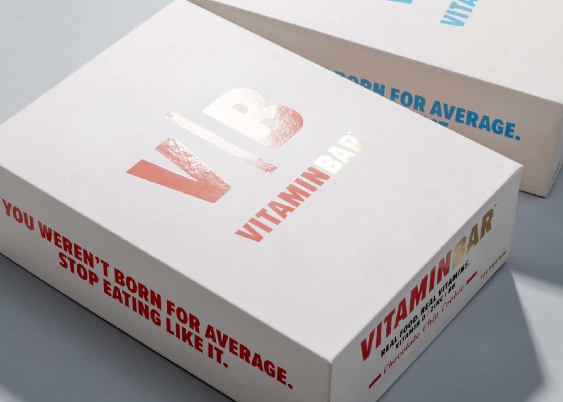 Two stacked white Vitamin Bar boxes displaying foil logos and bold motivational text along the sides.