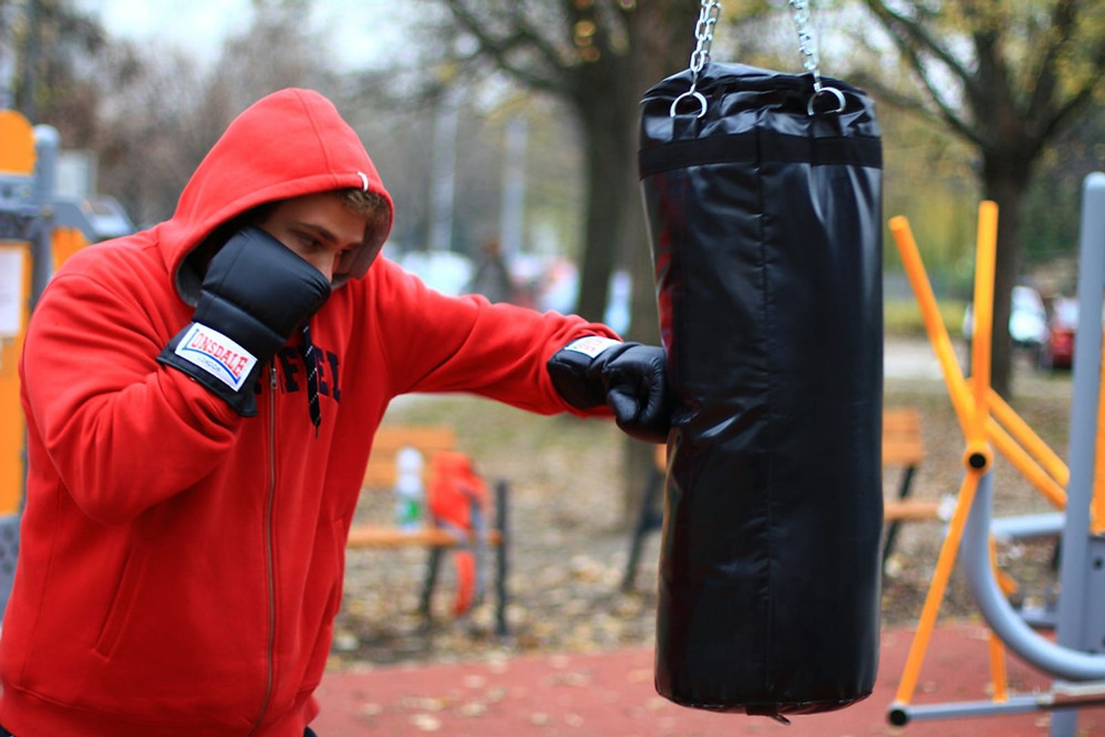 Boxer in a red hoodie hitting a heavy punching bag at an outdoor gym