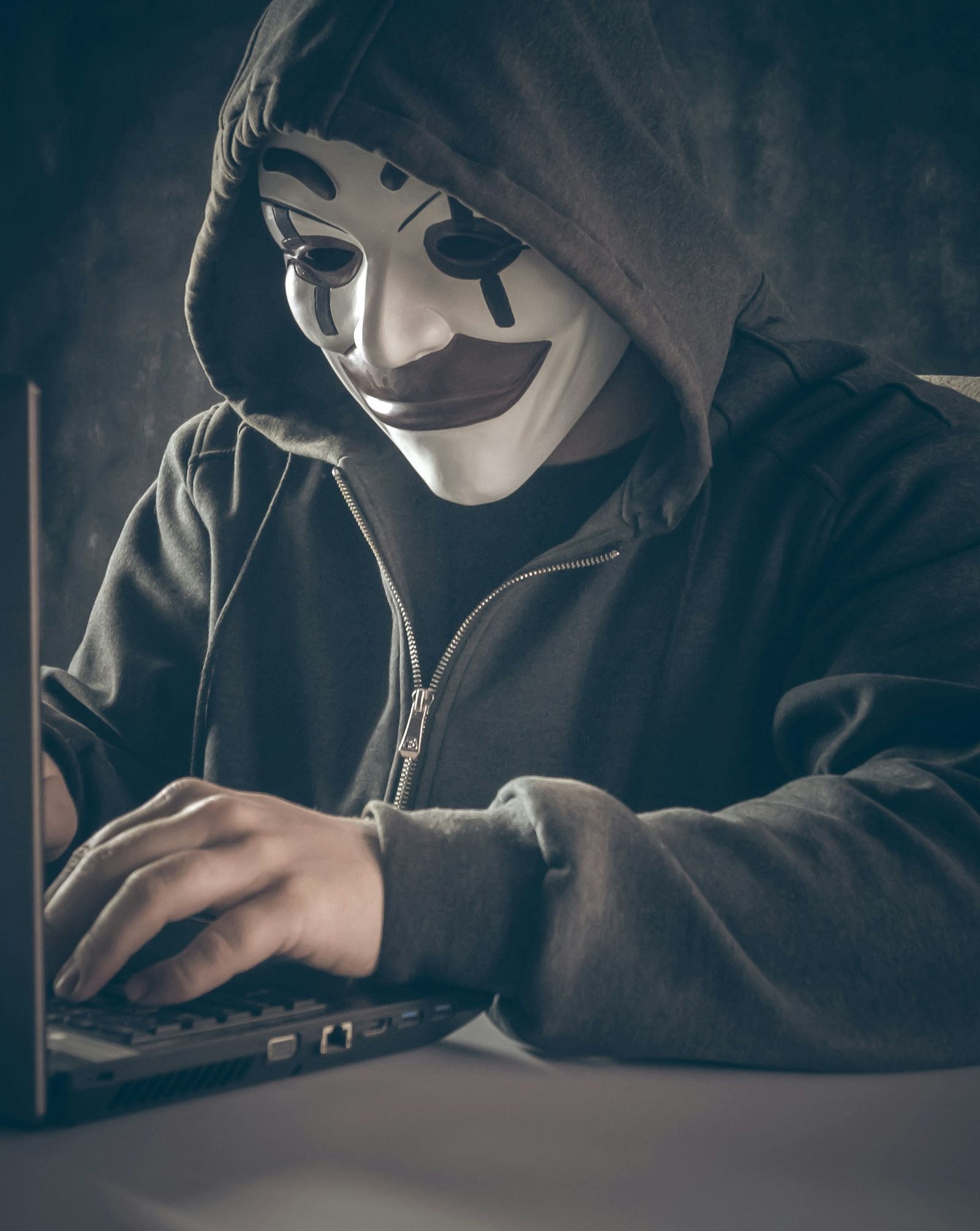 Person in a hooded top and white mask typing on a laptop