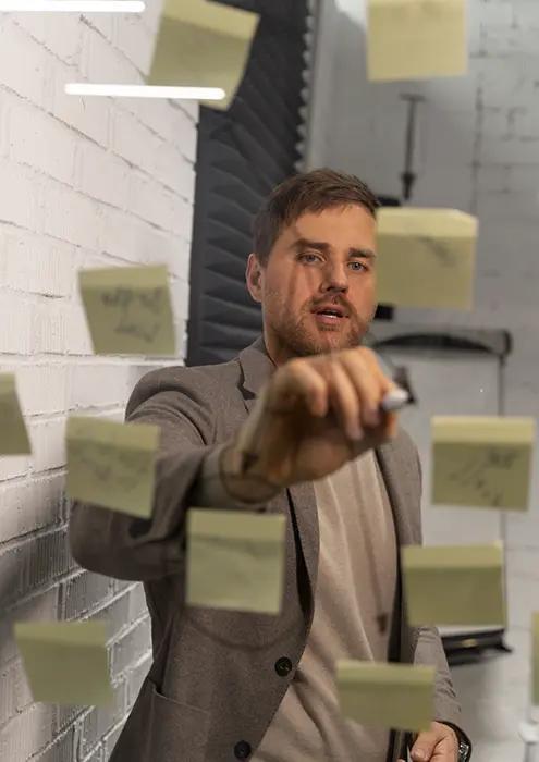 Confident businessman in a modern office presenting strategy with sticky notes, expressing dynamic planning and brainstorming concepts in a professional setting.