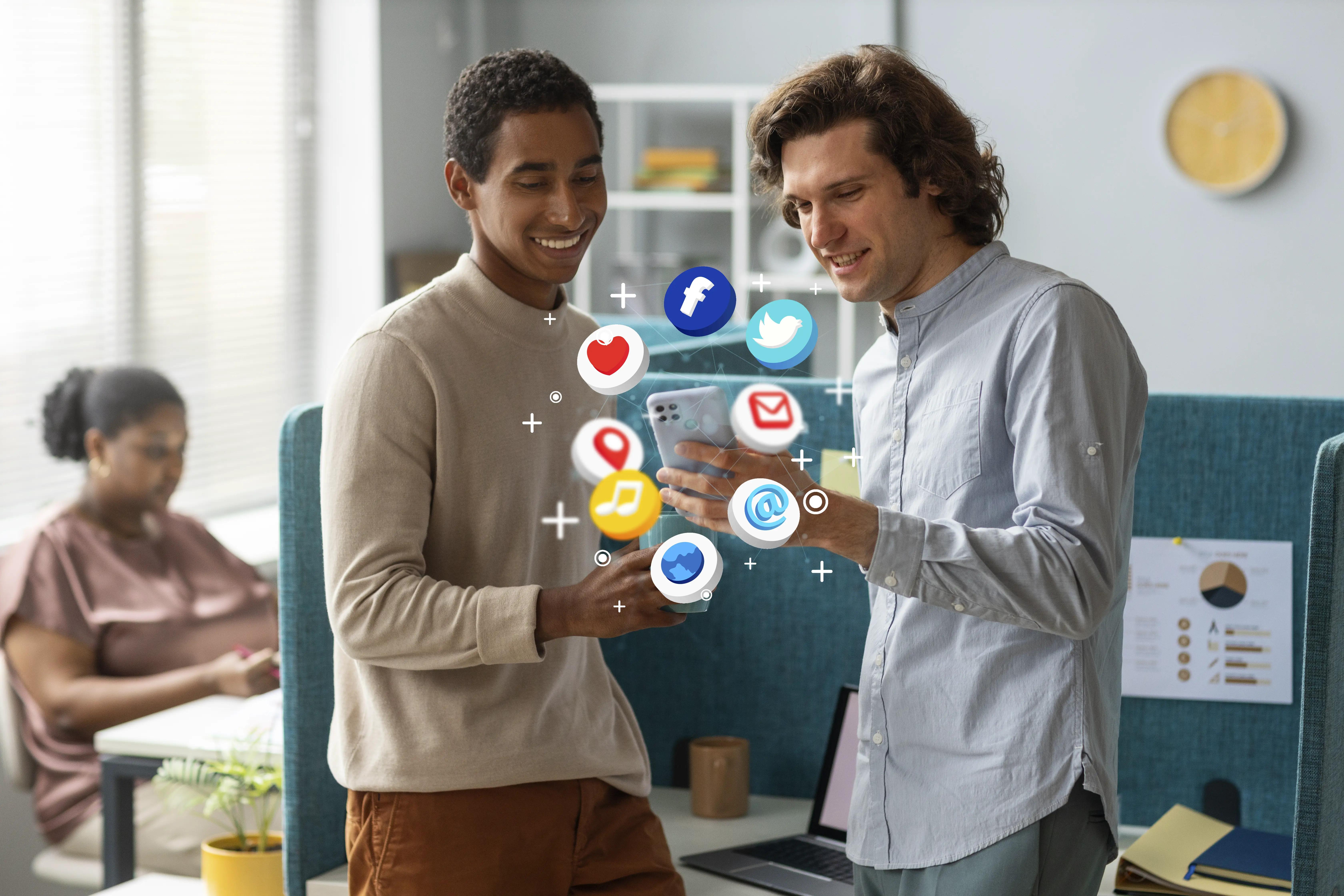 Two men engaging with a smartphone displaying various social media icons, suggesting a discussion on digital marketing strategies, in a modern office environment with a colleague working in the background
