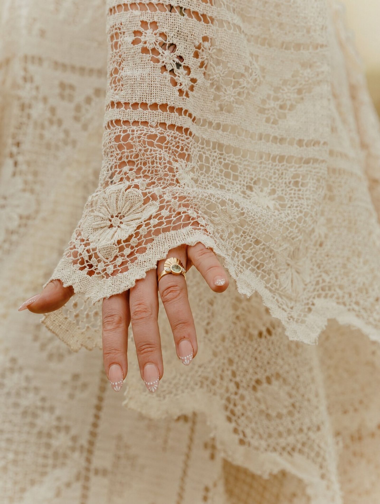 Close-up of the bride's lace sleeve and her hand, wedding ring on her finger