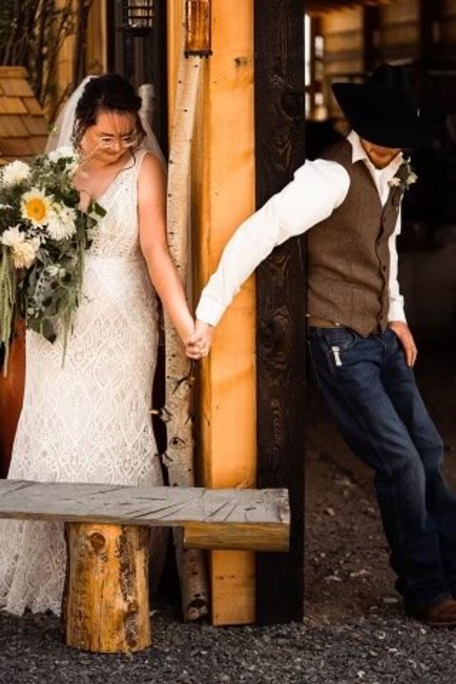 A bride and groom hold hands around a timber post before the ceremony, eyes closed, not yet looking at each other