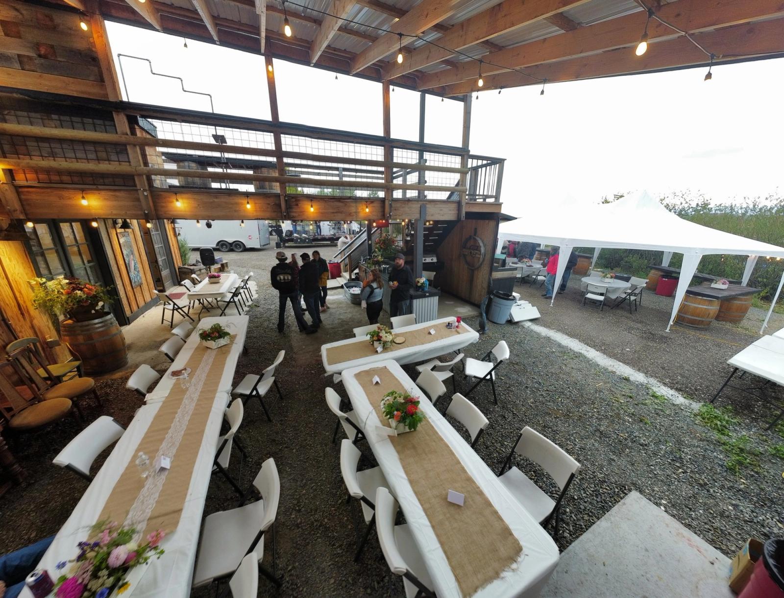 Reception tables with burlap runners and farm bouquets set under the Bourbon Barn deck, string lights above
