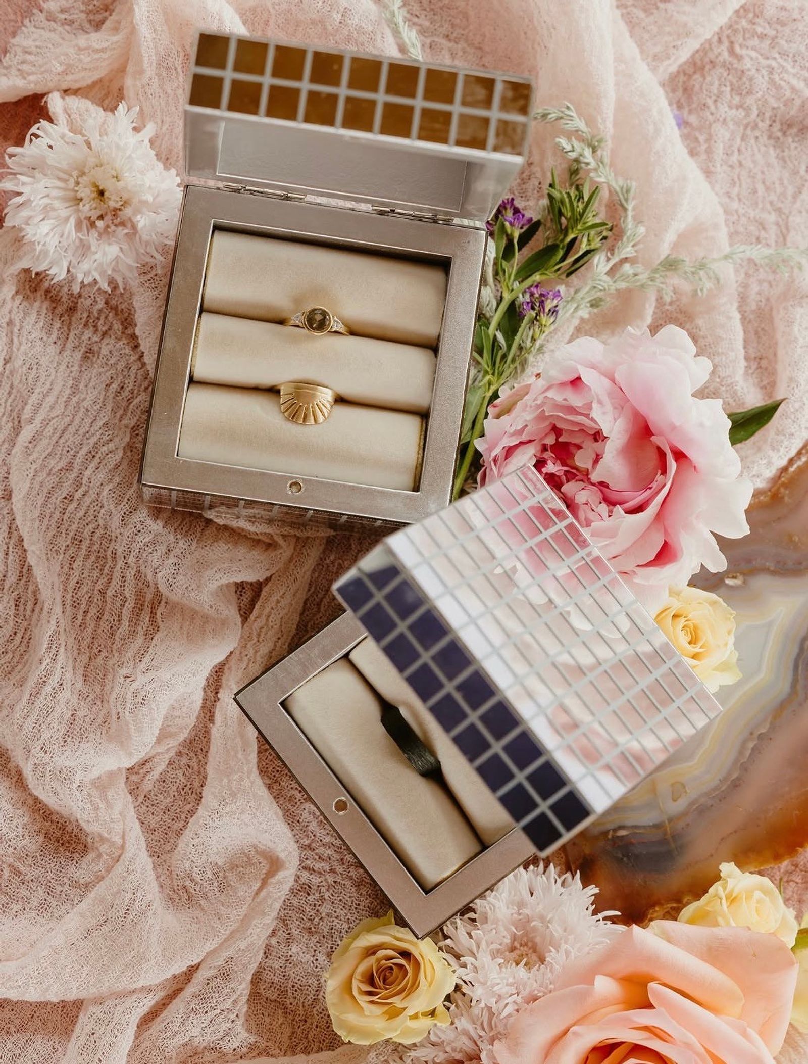 Wedding rings in mirrored boxes on soft pink linen with peonies and garden roses