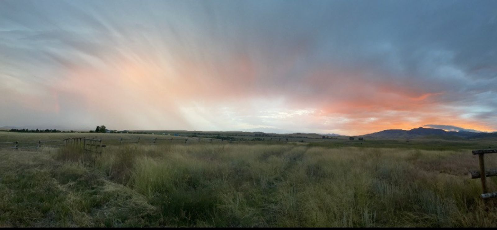 A wide view of rain and sunset light over the pasture and jackleg fence