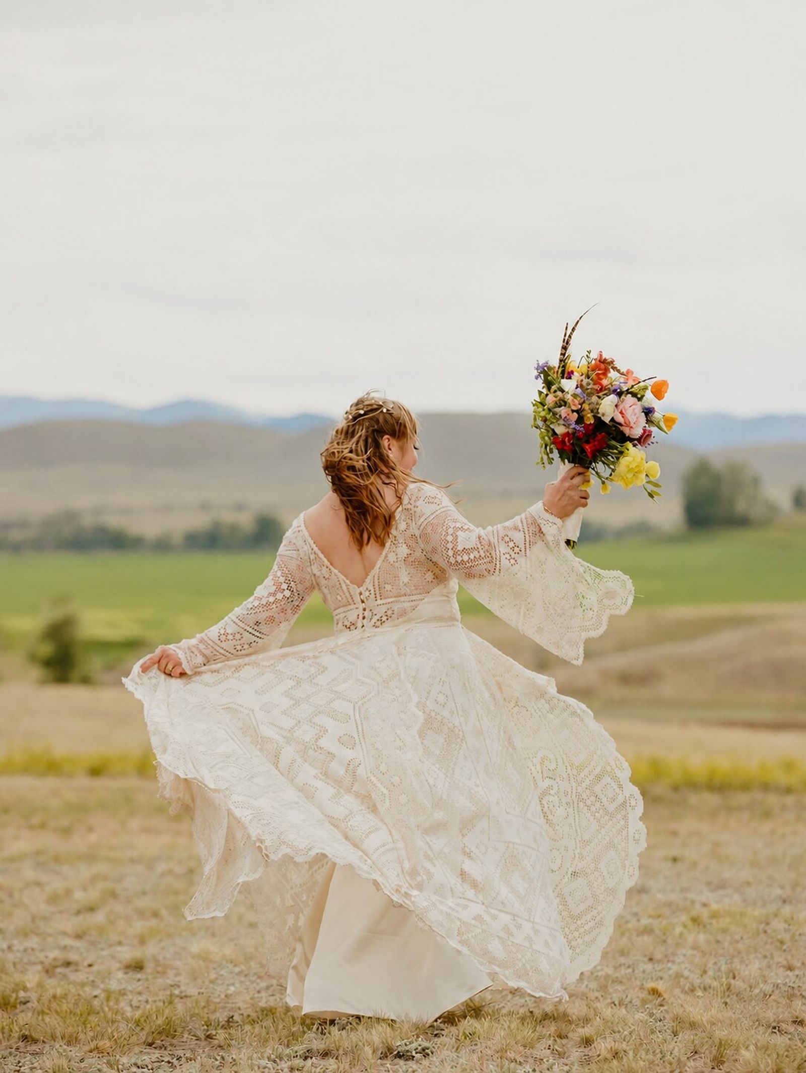 A bride twirls in her lace gown, bouquet raised, the valley and hills beyond