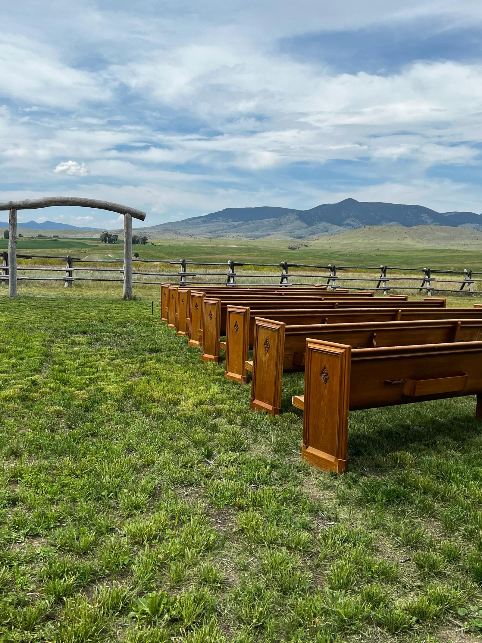 Rows of handcrafted wooden pews facing the log arch in the Ceremony Meadow
