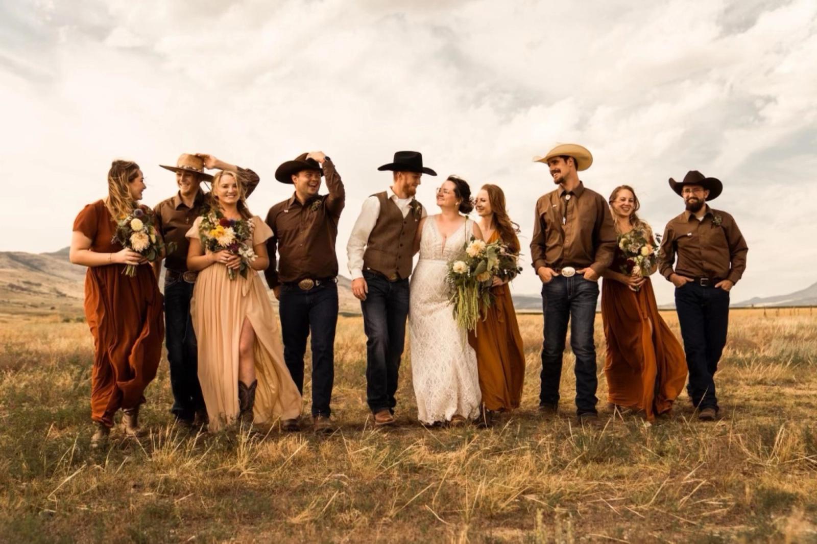 A wedding party in western wear - cowboy hats, rust-colored dresses and wildflower bouquets - walking through the prairie