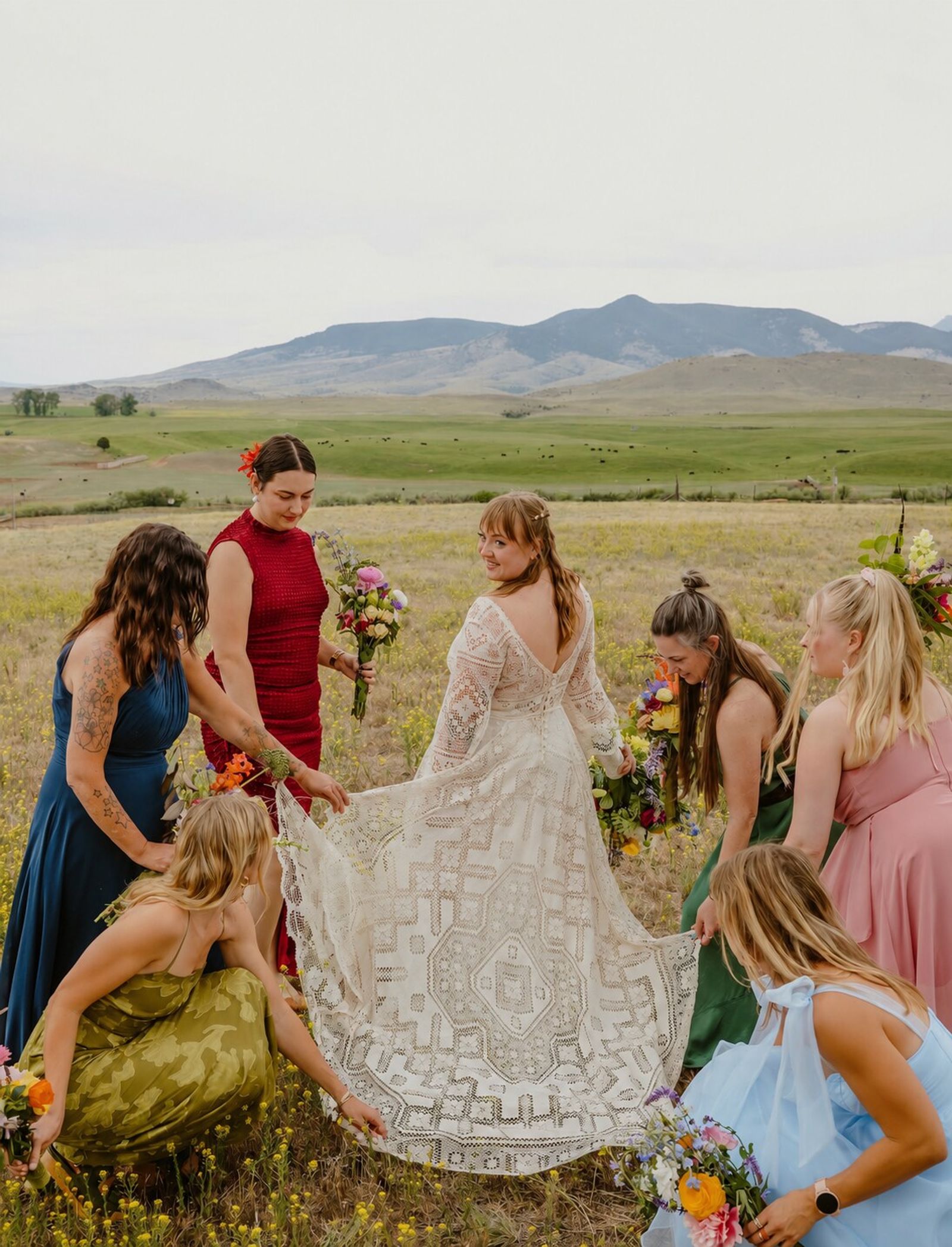 Bride and bridal party gathered in the meadow with mountains behind