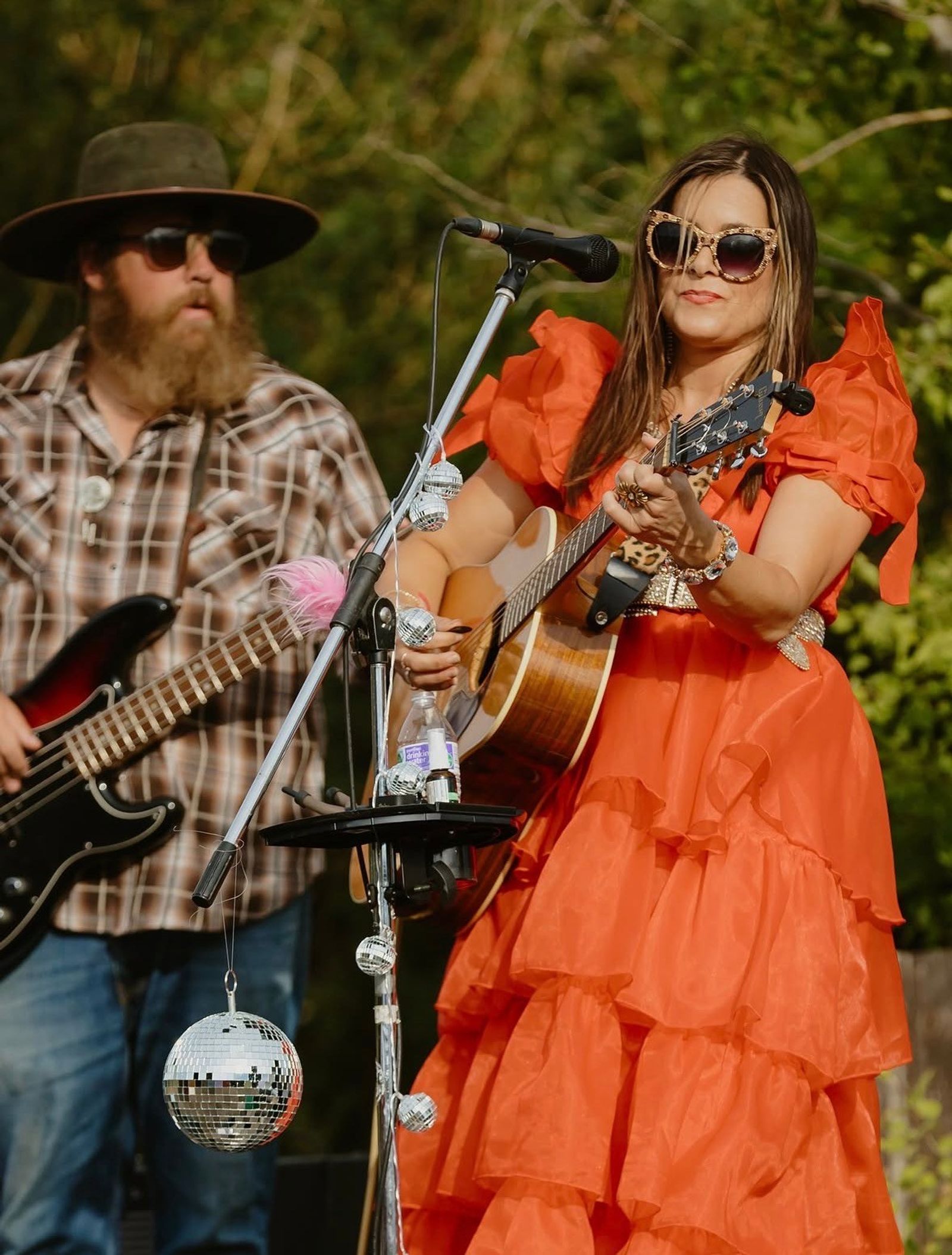 The singer in an orange ruffled dress plays acoustic guitar beside the bass player